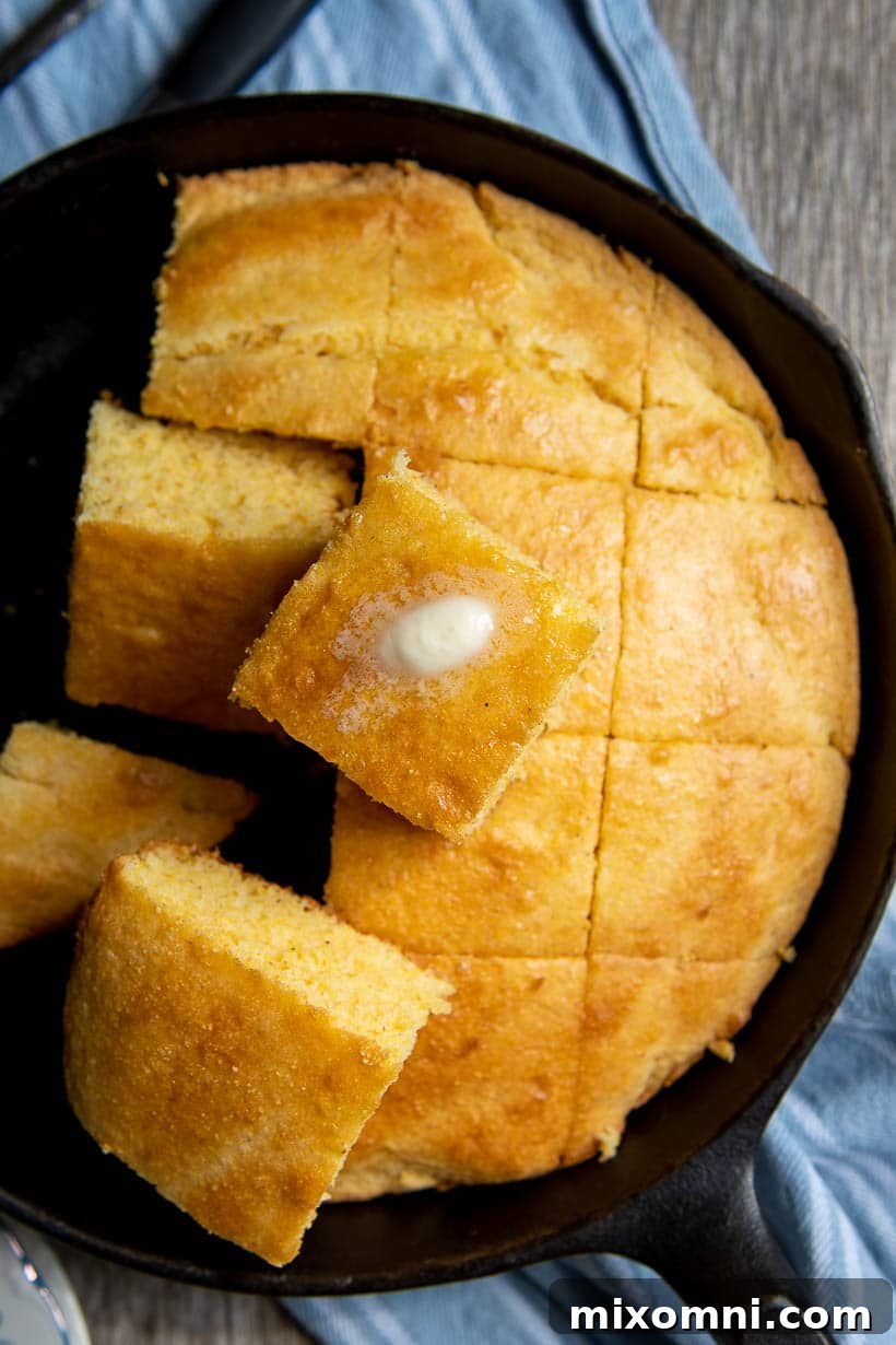 An overhead shot of an iron skillet filled with freshly cut cornbread, with a piece of melting butter on top, ready to serve.