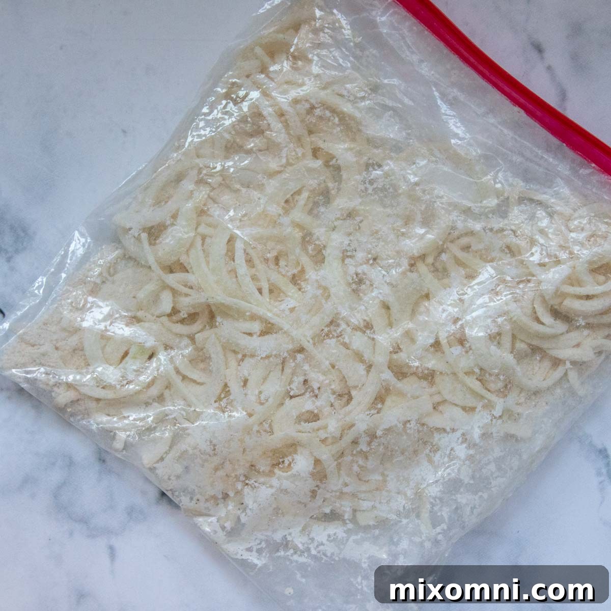 A clear ziplock bag filled with flour-coated onion slices, perfectly prepped and ready for frying to achieve their ultimate crispness.