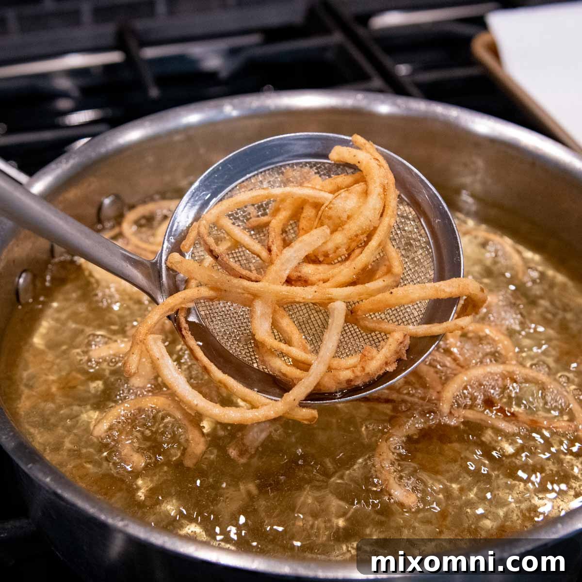 Golden-brown, crispy fried onions being delicately lifted from the hot oil with a wire skimmer, ready to drain.