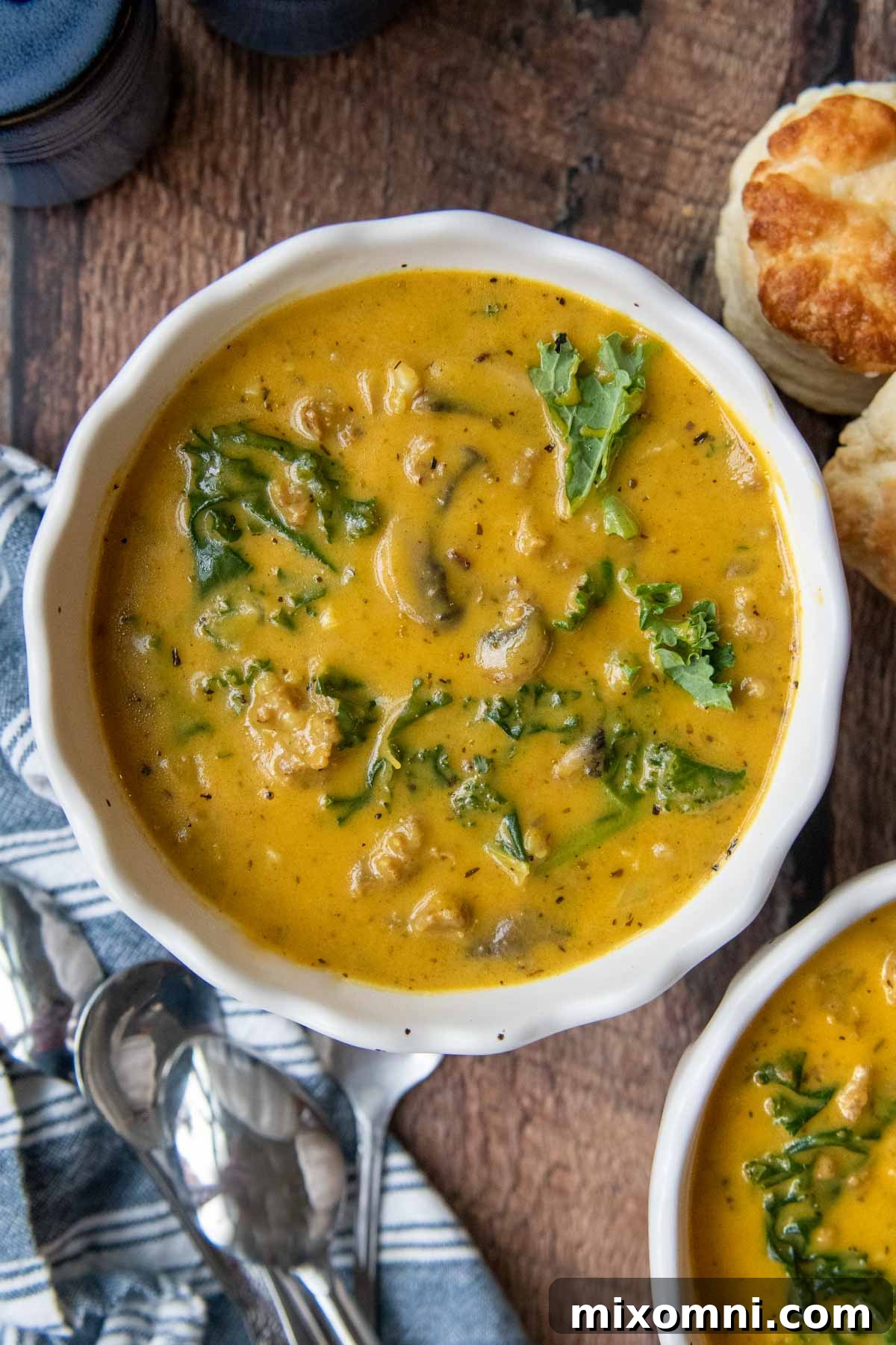 An overhead shot of a vibrant bowl of pumpkin sausage soup, rich with pumpkin and visible pieces of sausage and kale, served in a white bowl with a spoon, ready to be enjoyed.