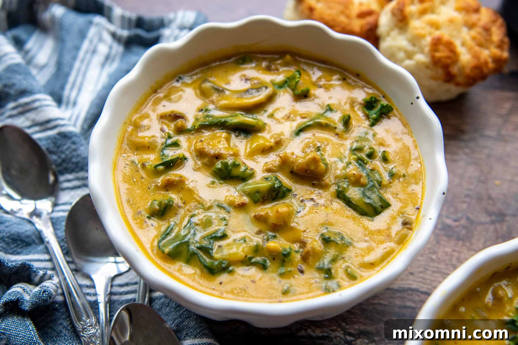 A horizontal view of two white soup bowls, one filled with pumpkin sausage soup and the other empty, set on a dark surface, highlighting the rich texture of the soup.