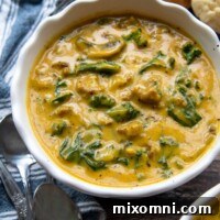 a bowl of pumpkin soup with a blue napkin and biscuits in the background