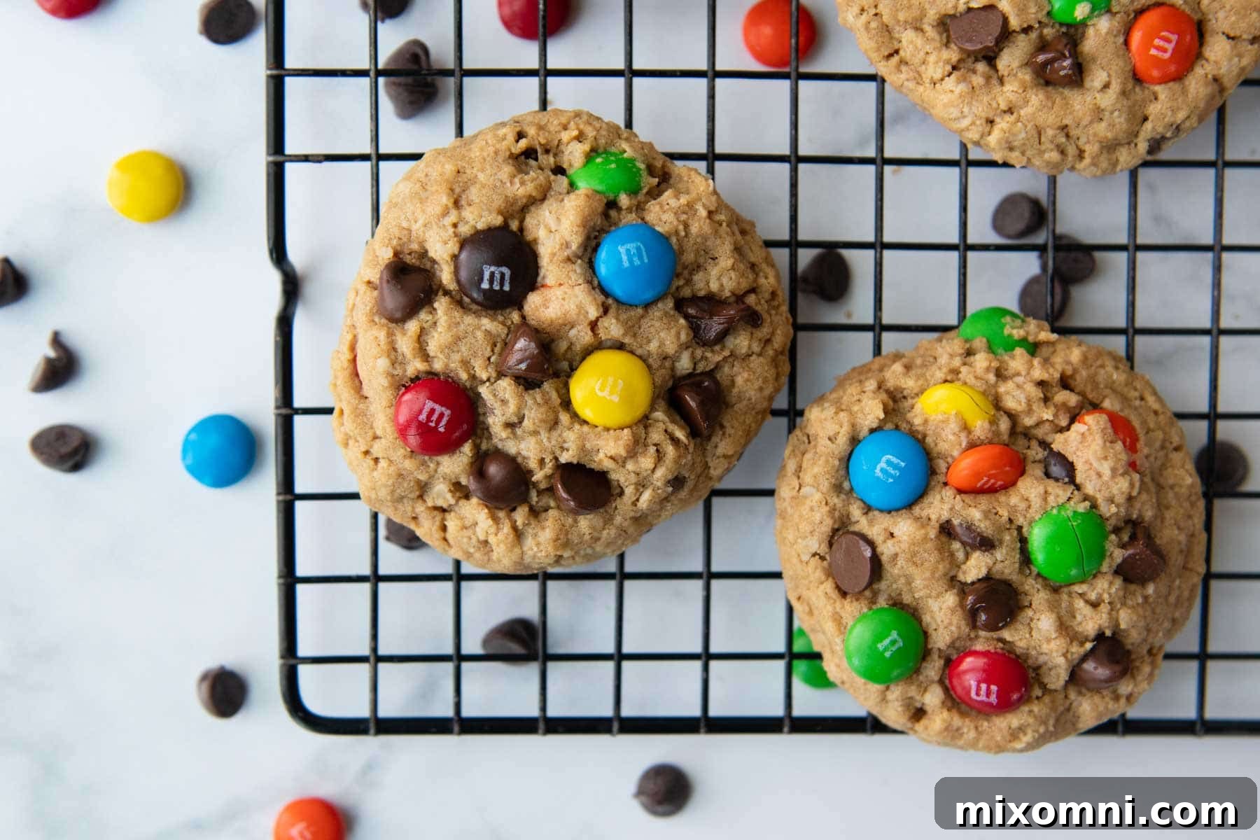 A collection of freshly baked gluten-free monster cookies cooling on a wire rack, surrounded by scattered M&M candies, emphasizing their colorful and delicious appeal.