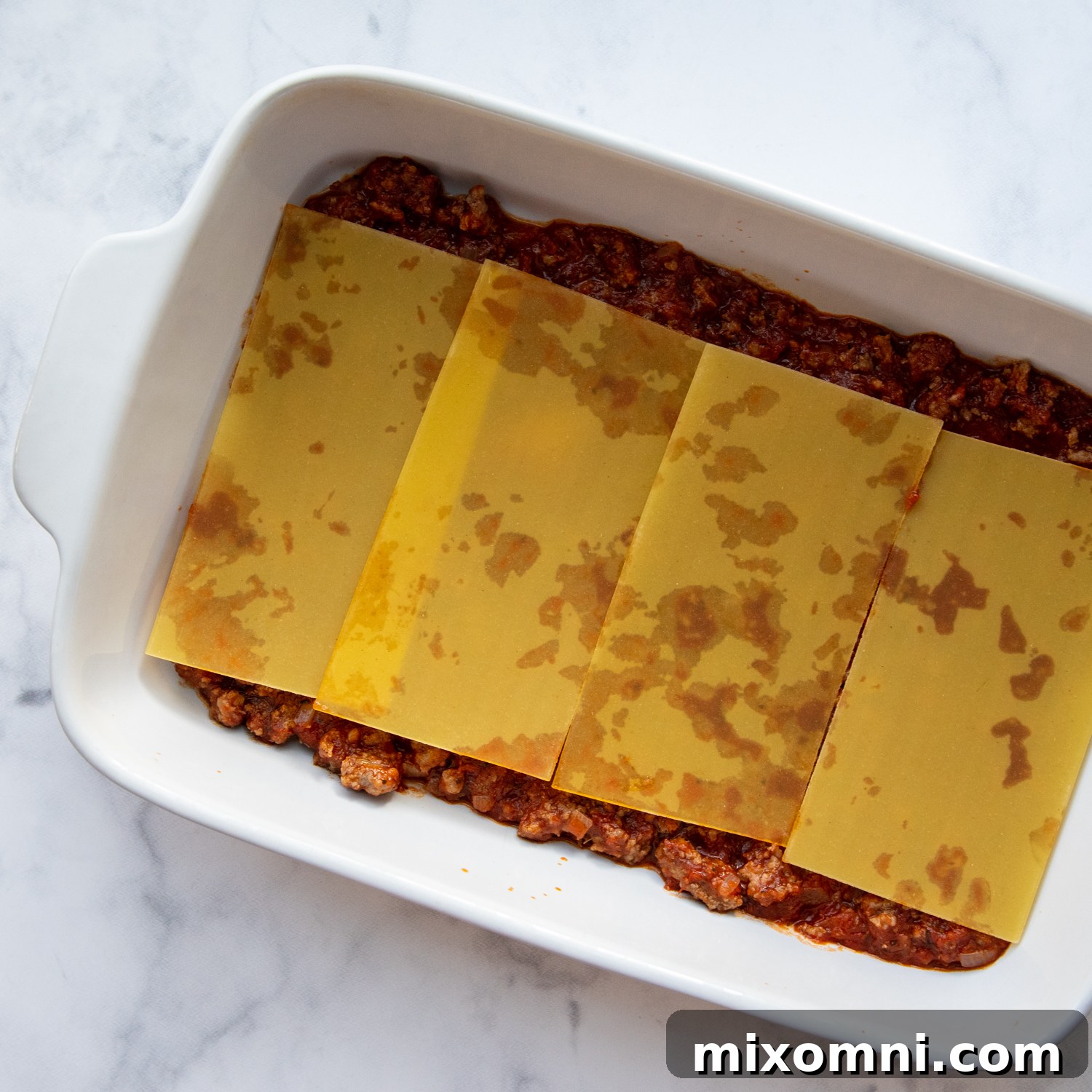 Step-by-step images illustrating the careful layering of gluten-free lasagna noodles, ricotta cheese, and savory meat sauce in a baking dish.