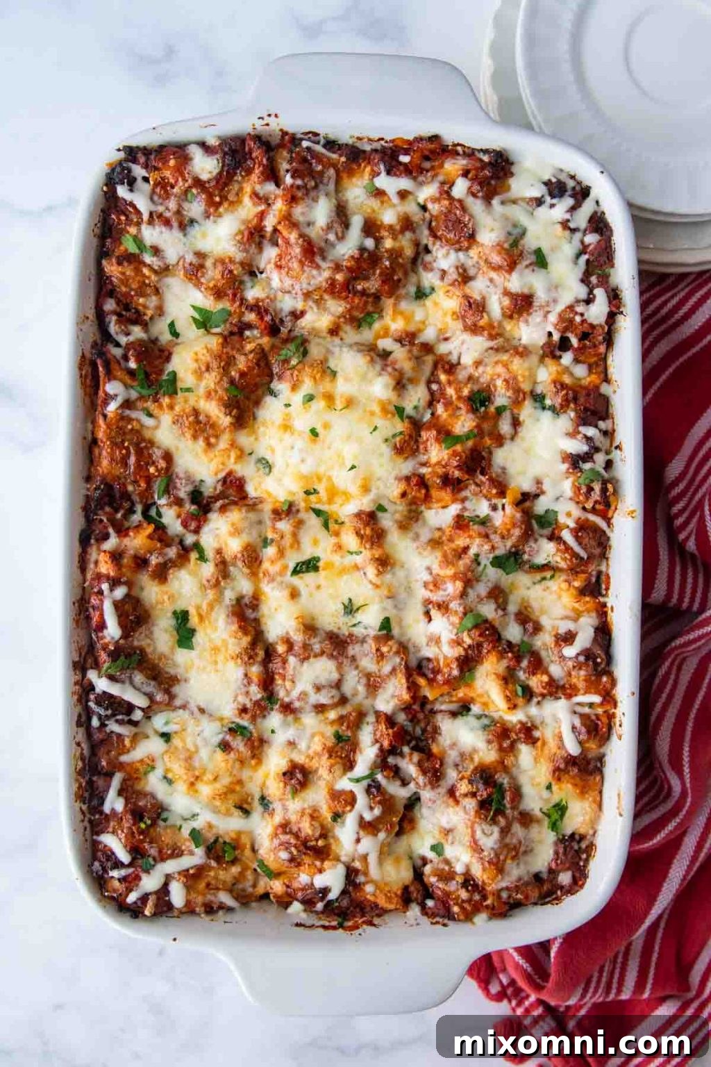 An inviting overhead shot of a freshly baked gluten-free lasagna in a pristine white dish, accompanied by a rustic red kitchen towel, highlighting its warm, comforting appeal.
