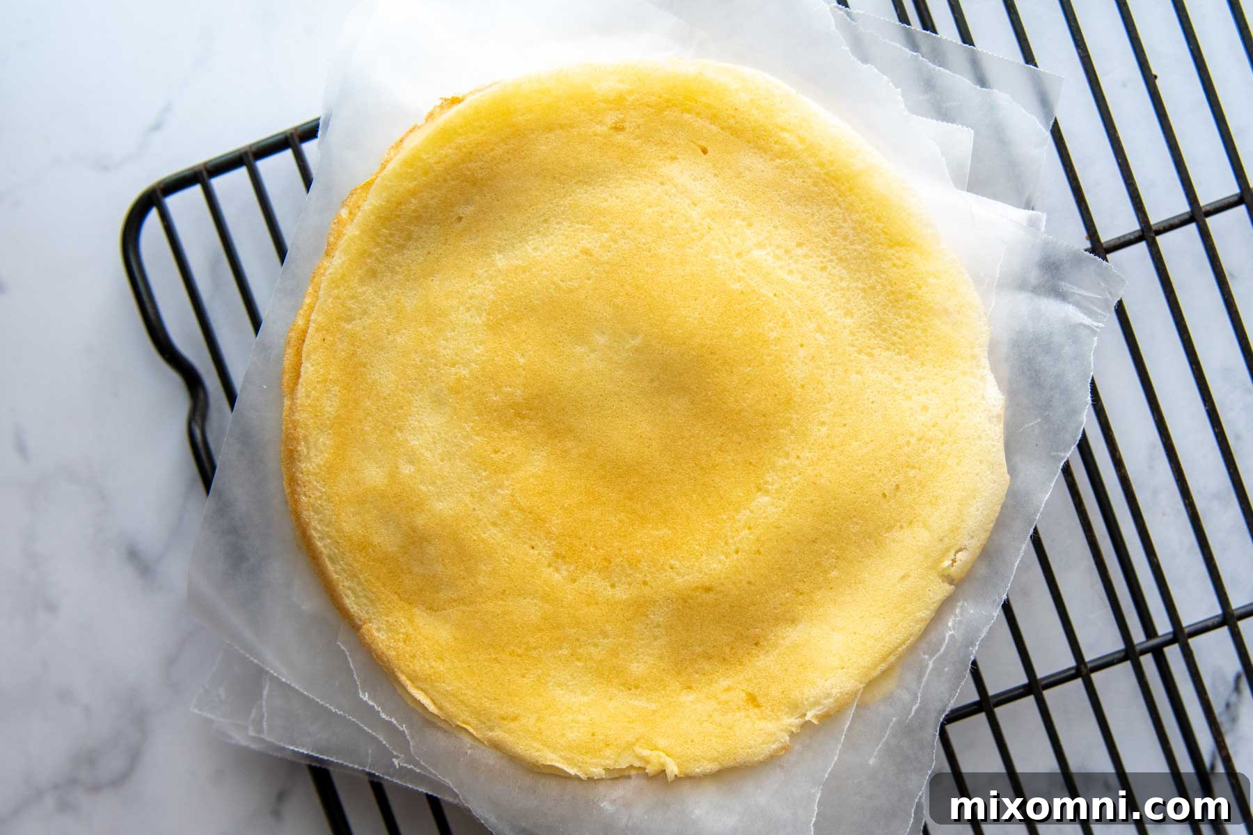 Cooked gluten-free crepes neatly stacked on a cooling rack with wax paper separating each layer.