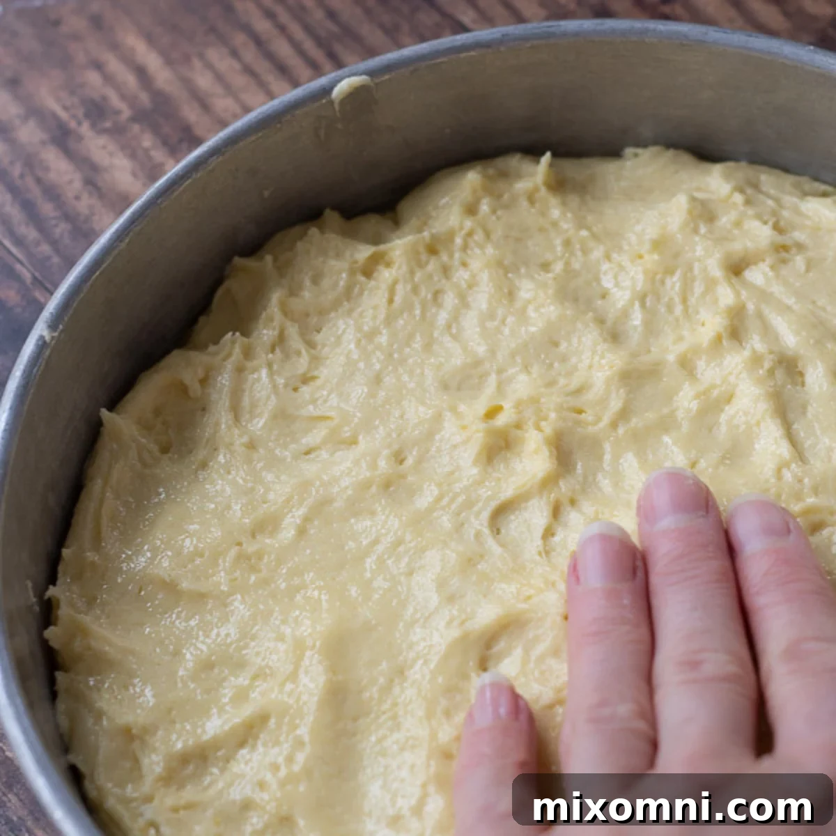 Fingers pressing the thick cake batter evenly into a cake pan.