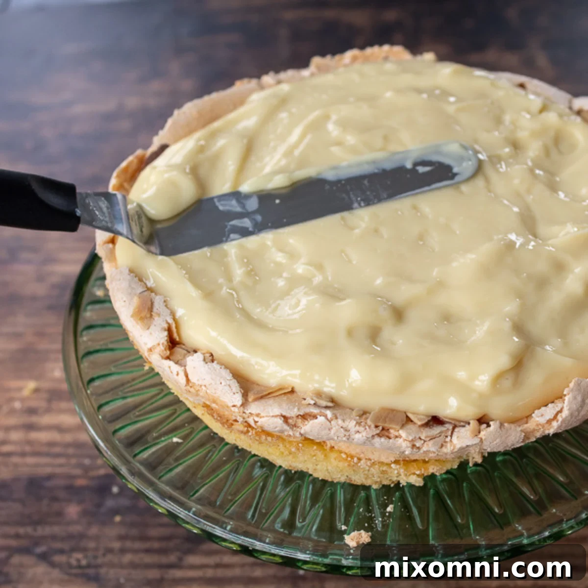 Creamy custard filling being spread over a baked cake layer with meringue.