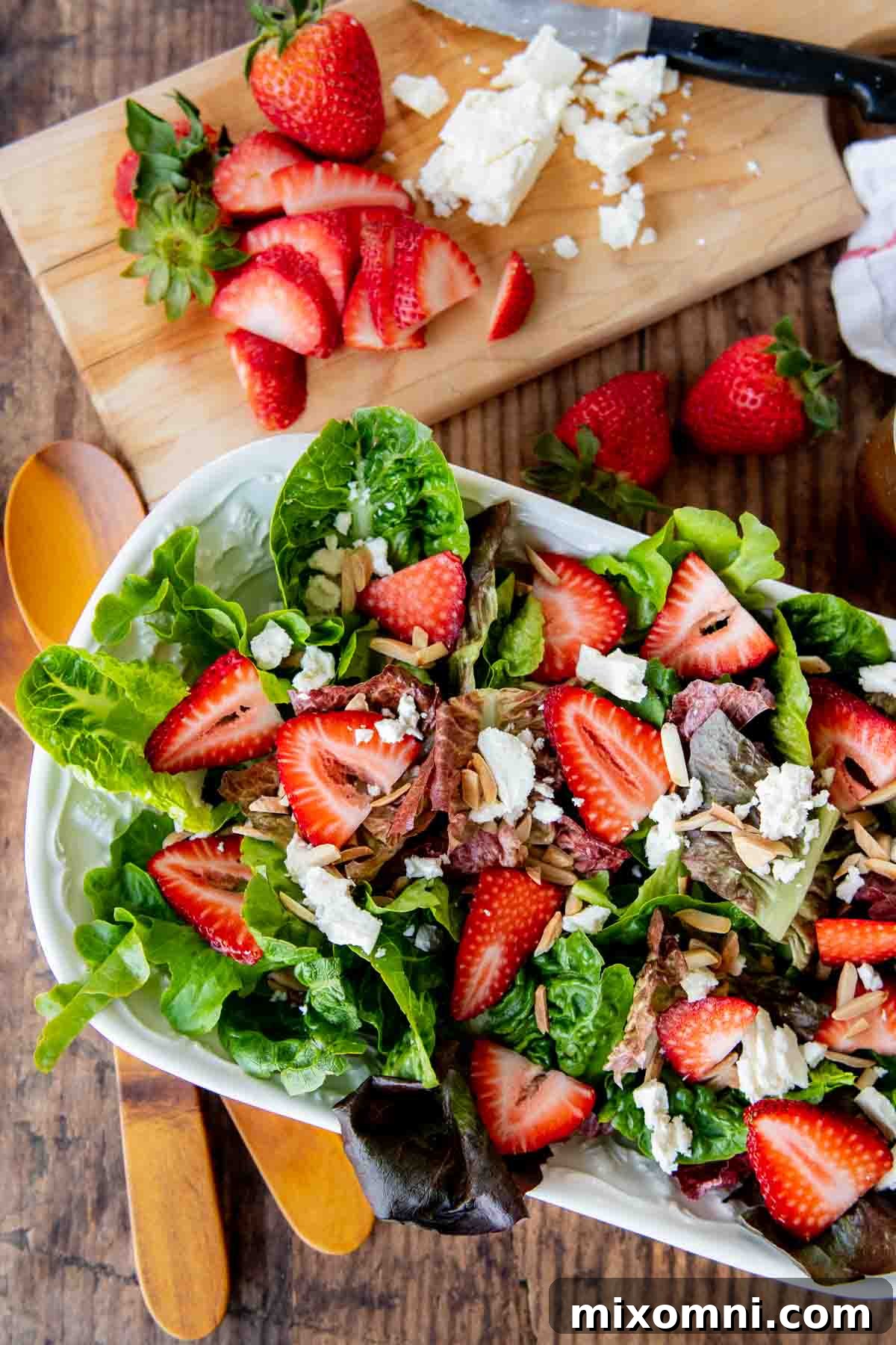 An overhead view of a vibrant strawberry green salad with crumbled feta cheese, toasted nuts, and a light vinaigrette, offering a delightful mix of sweet, savory, and tangy flavors.