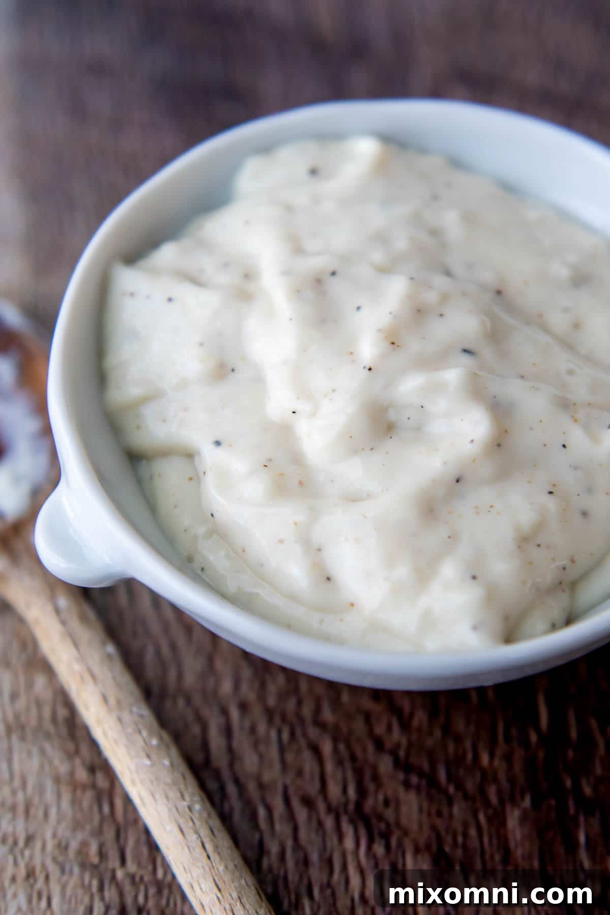 close up of gluten-free chicken soup in a white bowl with wooden spoon next to it