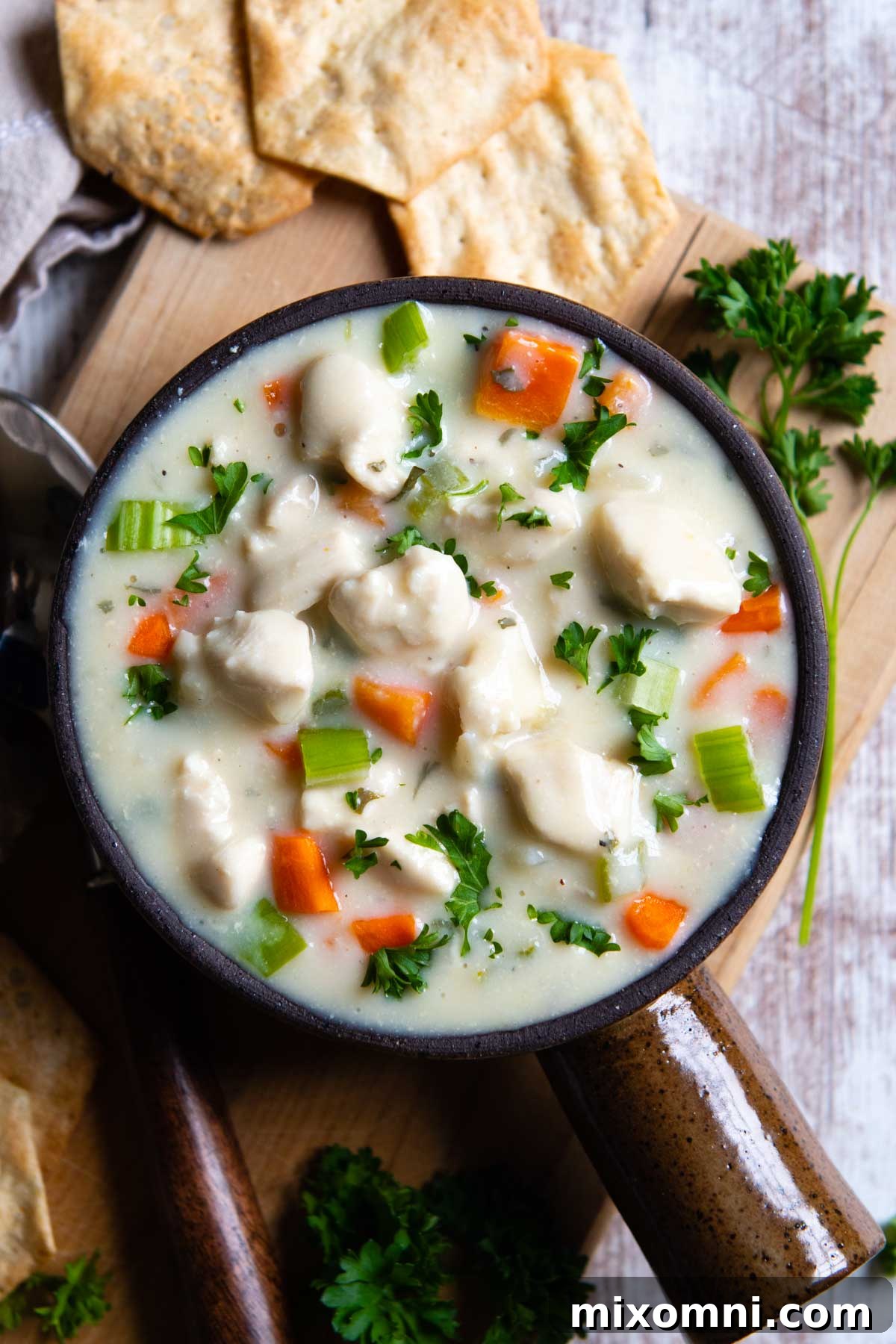 overhead shot of chicken soup in a brown bowl with a handle and crackers laying next to it