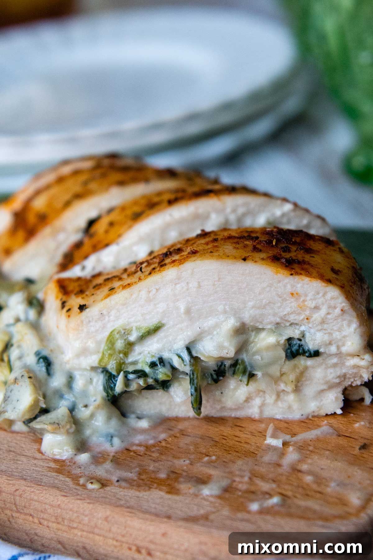 Close-up of a perfectly sliced spinach artichoke stuffed chicken breast revealing the creamy filling on a rustic wooden cutting board, ready to serve.