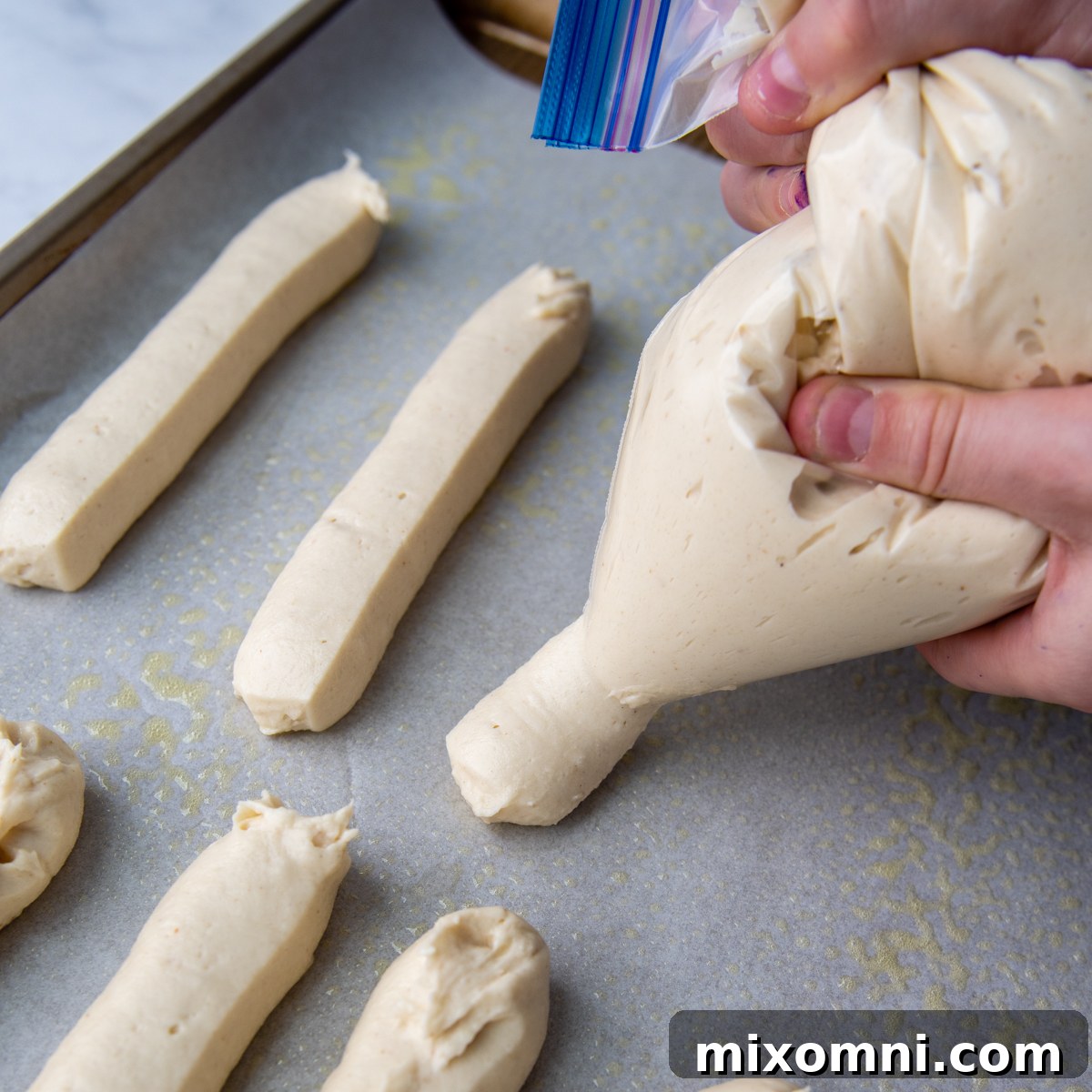 Piping the breadstick dough onto a baking sheet using a modified plastic Ziploc bag.