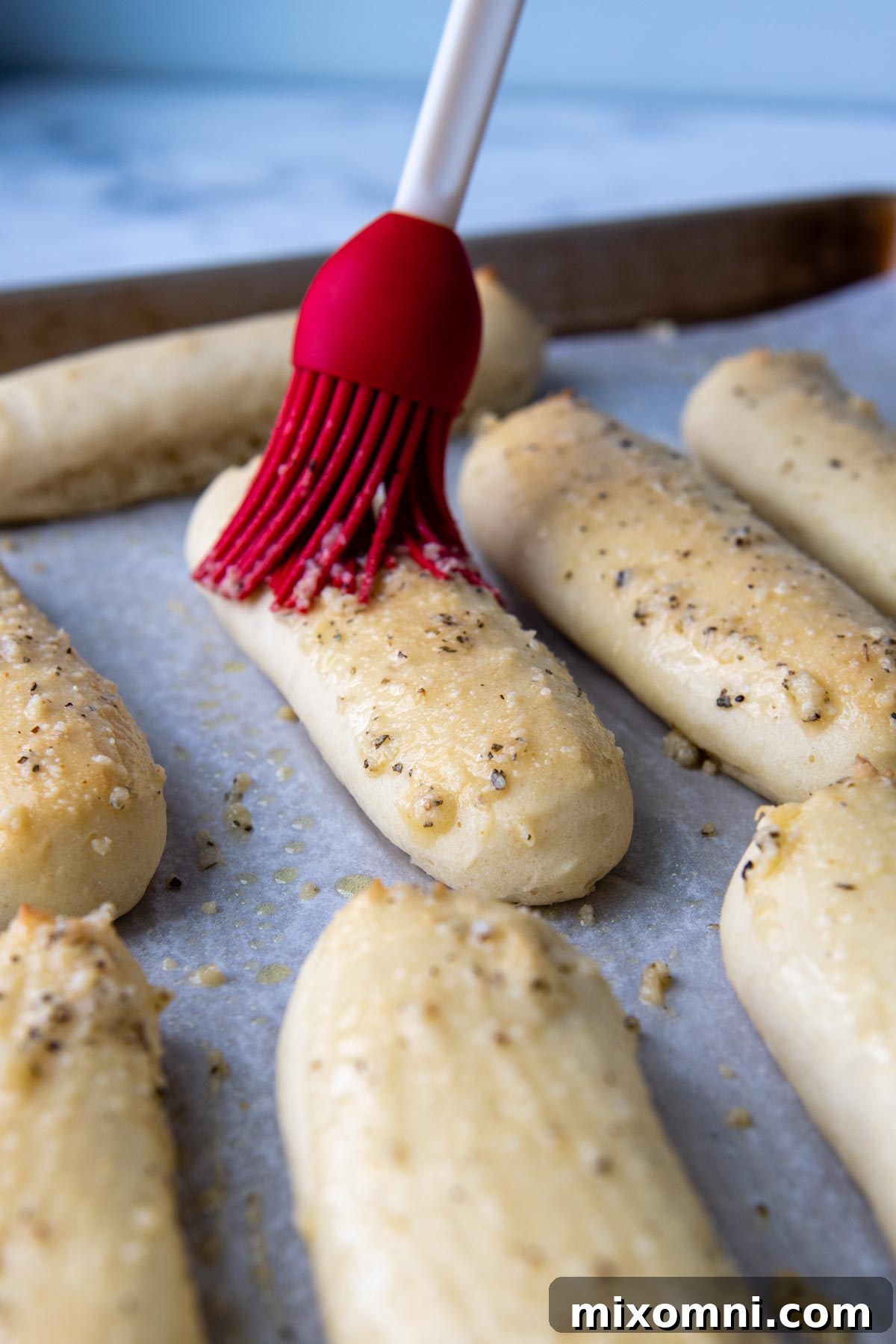 A pastry brush applying melted butter and garlic topping onto hot, freshly baked gluten-free breadsticks.
