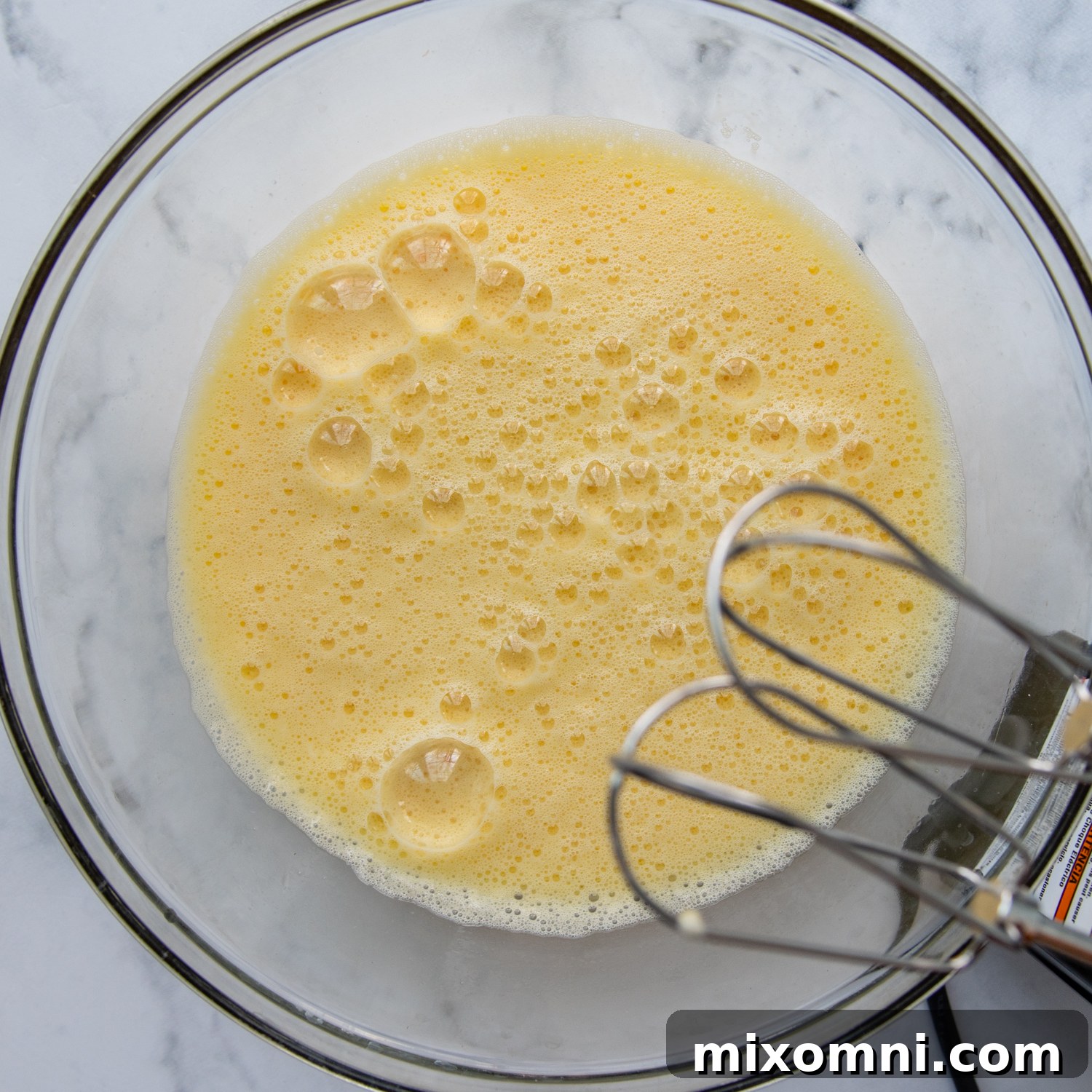 Eggs being beaten to a frothy consistency in a large mixing bowl, highlighting the air incorporated for a light casserole.
