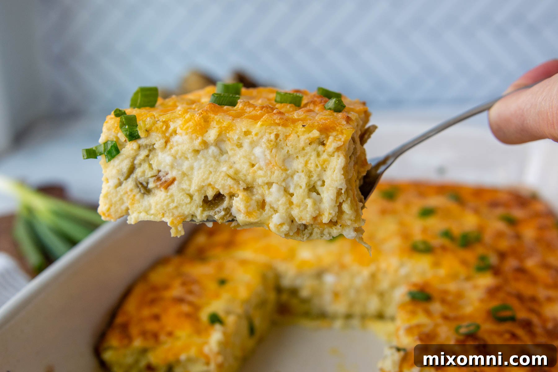 A close-up shot of a slice of green chile egg casserole being delicately lifted from the pan with a spatula, highlighting its rich textures.