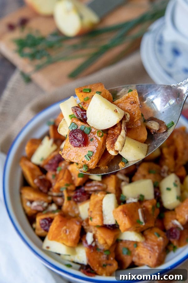 An antique silver spoon holding up a serving of sweet potato salad from a beautiful serving dish.