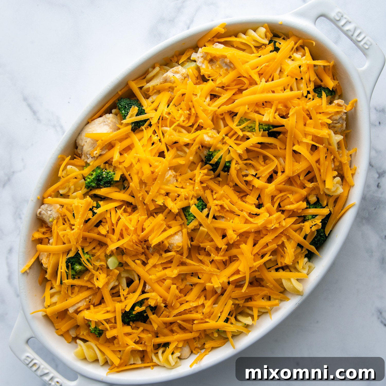 the unbaked casserole being assembled with cheese on top.