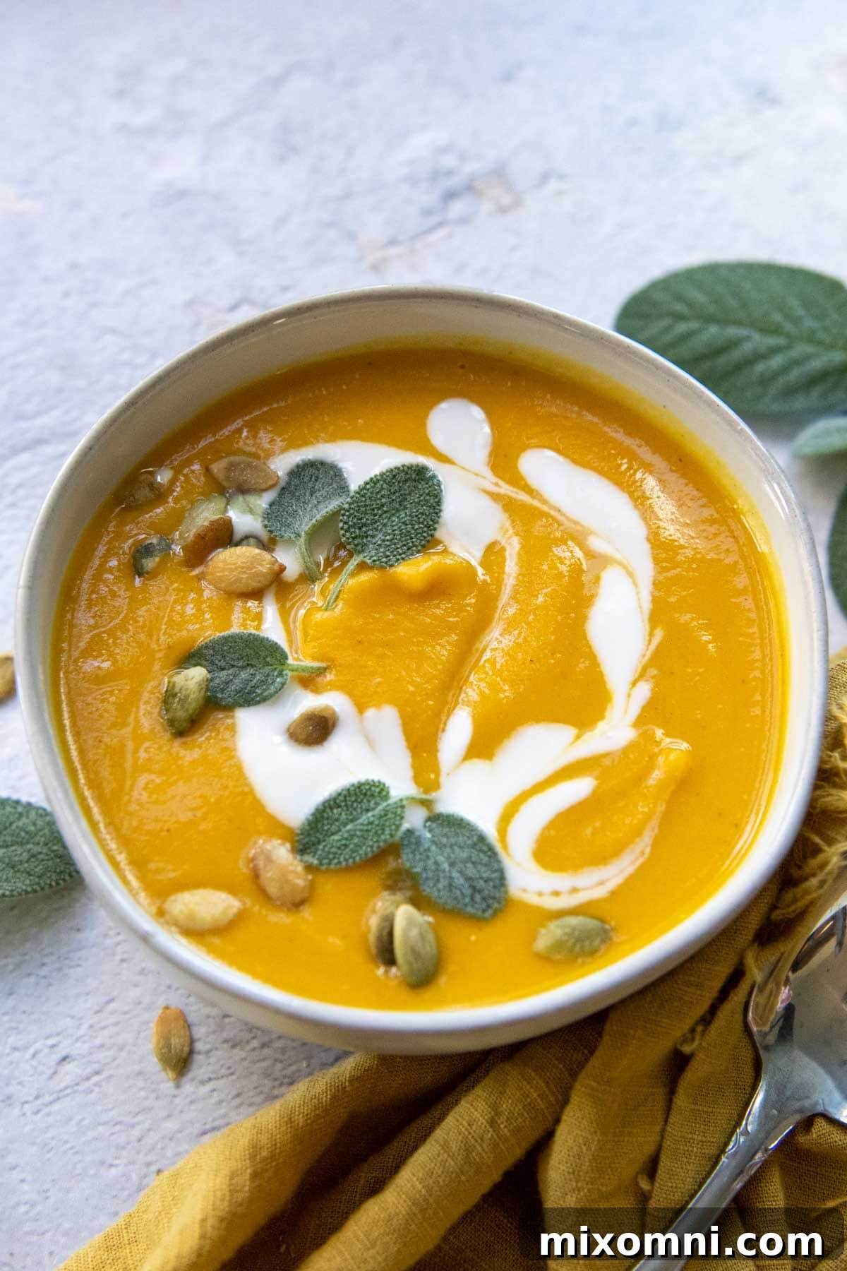 A bowl of creamy butternut squash soup, elegantly swirled with coconut milk and garnished with fresh sage leaves.