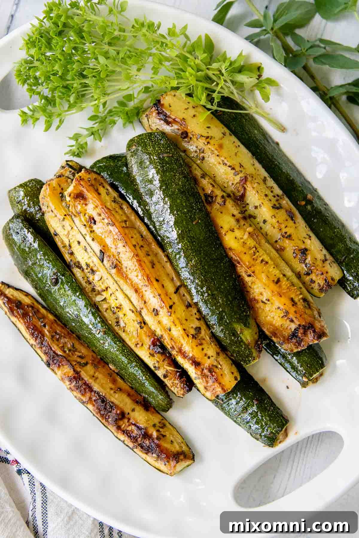 Crispy roasted zucchini pieces on a white plate, garnished with fresh herbs.