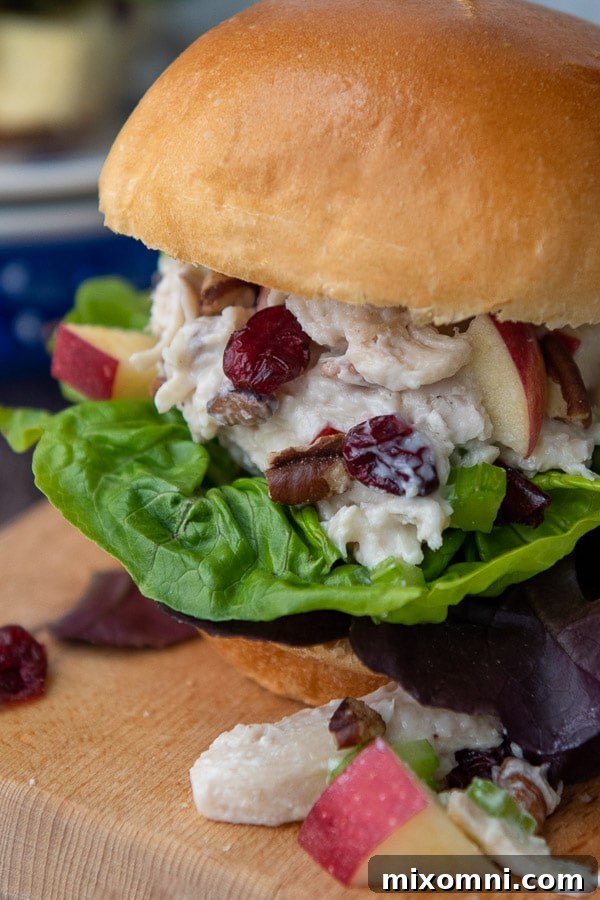 A generously filled chicken salad sandwich on a brioche bun, resting on a rustic wooden cutting board.