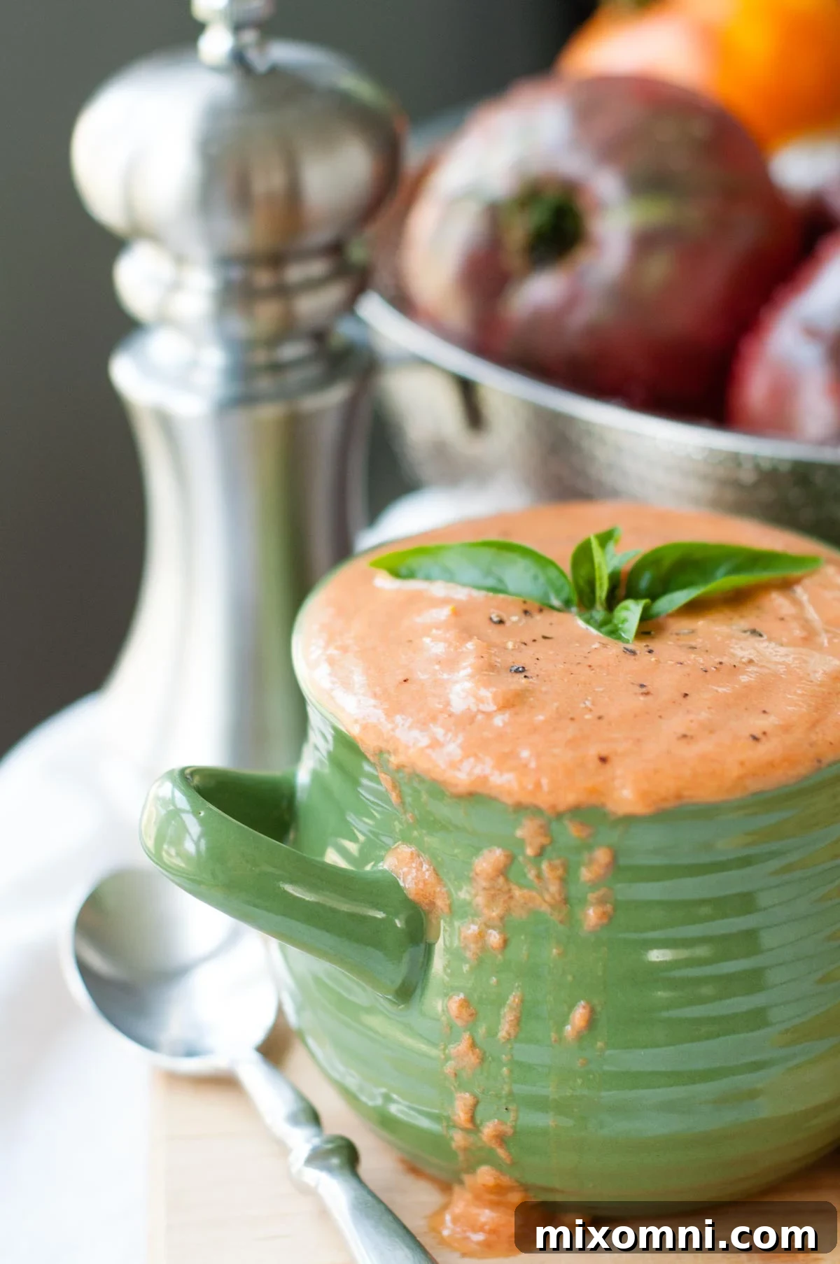 A comforting bowl of creamy roasted tomato soup, artfully garnished with fresh basil leaves.