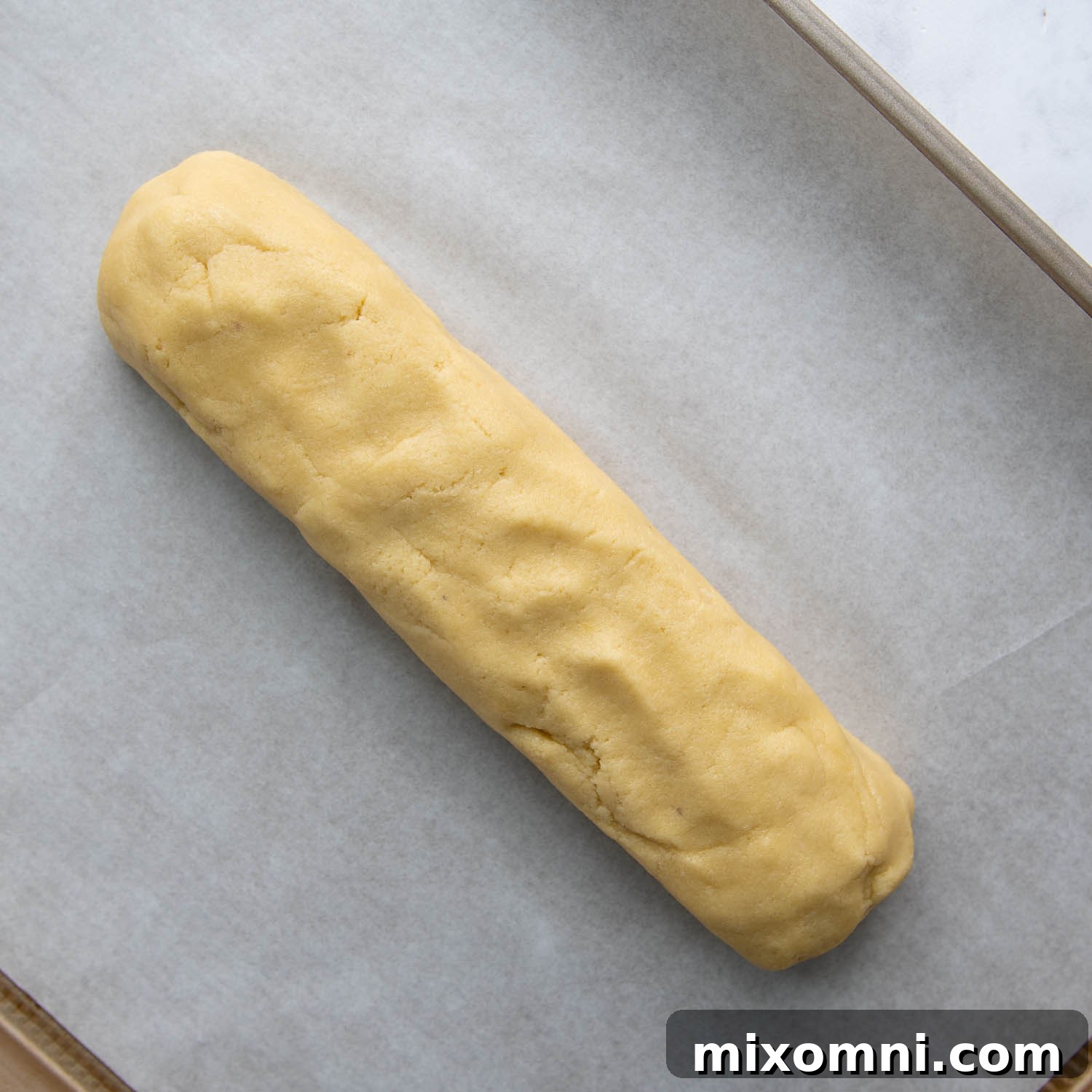 The biscotti dough shaped into a uniform log, ready for its first bake on a parchment-lined baking sheet.