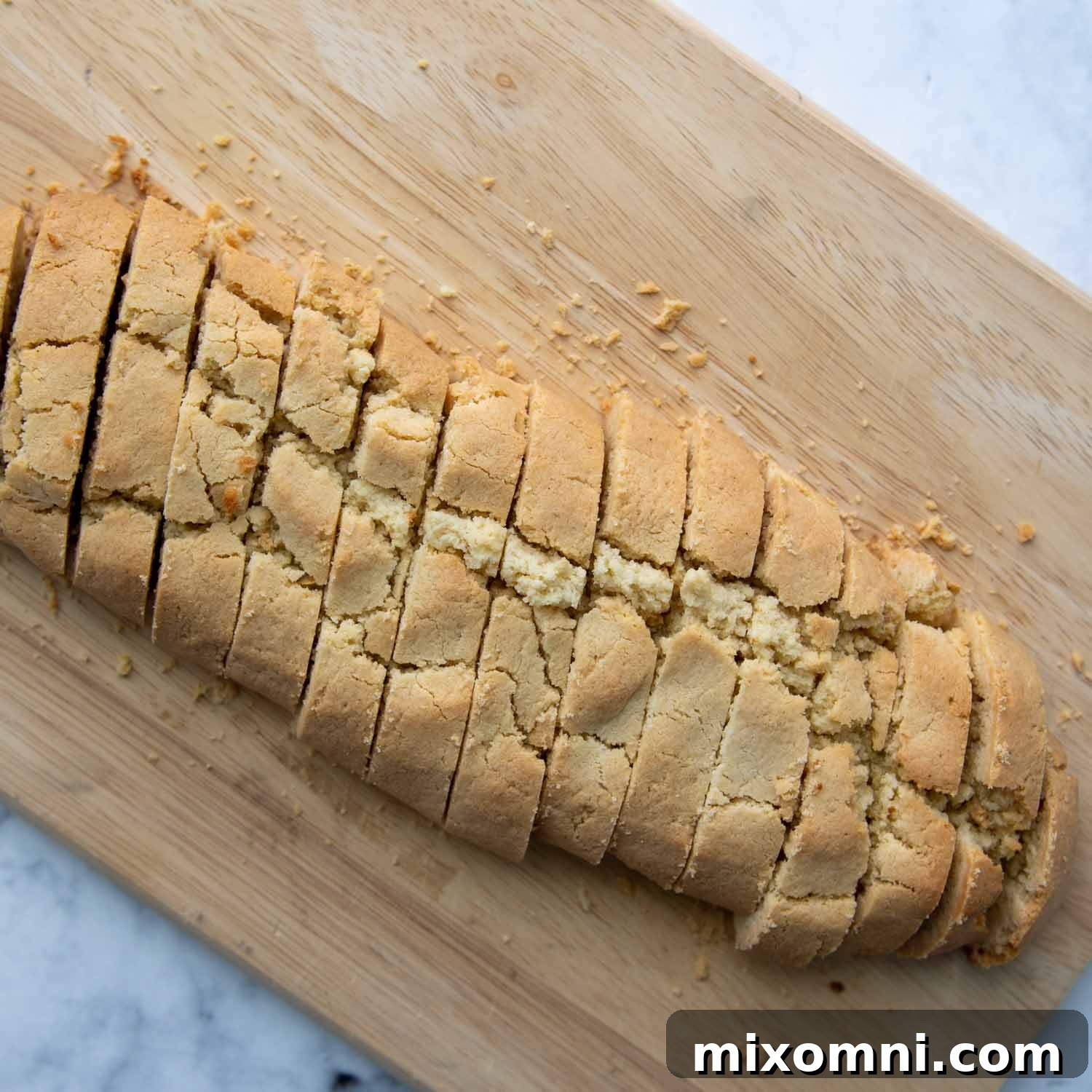 Diagonal slices of partially baked biscotti neatly arranged on a cutting board, ready for the second bake.