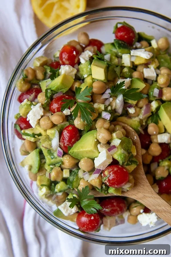 A wooden spoon lifting a vibrant serving of chickpea avocado salad, showcasing its fresh ingredients.
