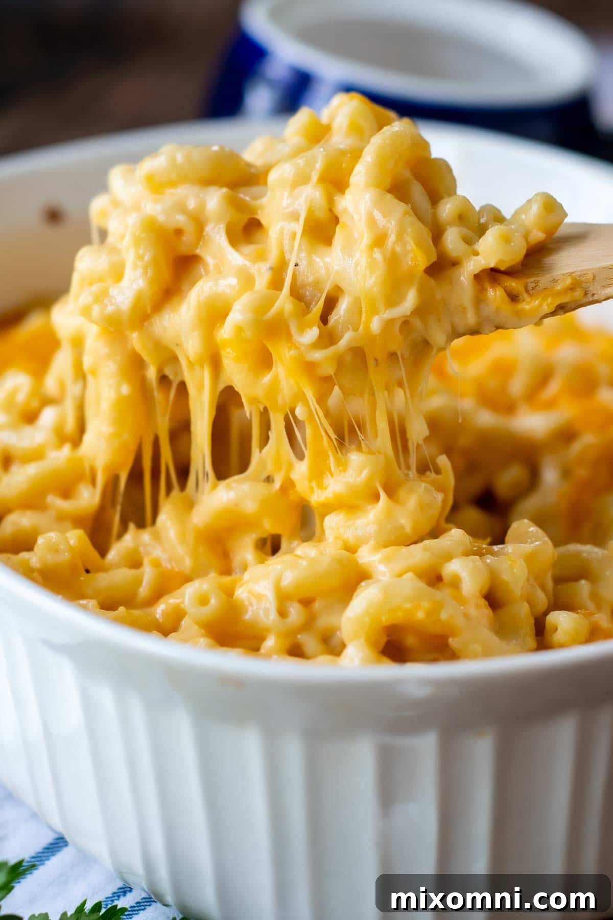 A wooden spoon lifting out a generous, cheesy serving of baked Velveeta mac and cheese, showcasing its rich creaminess.