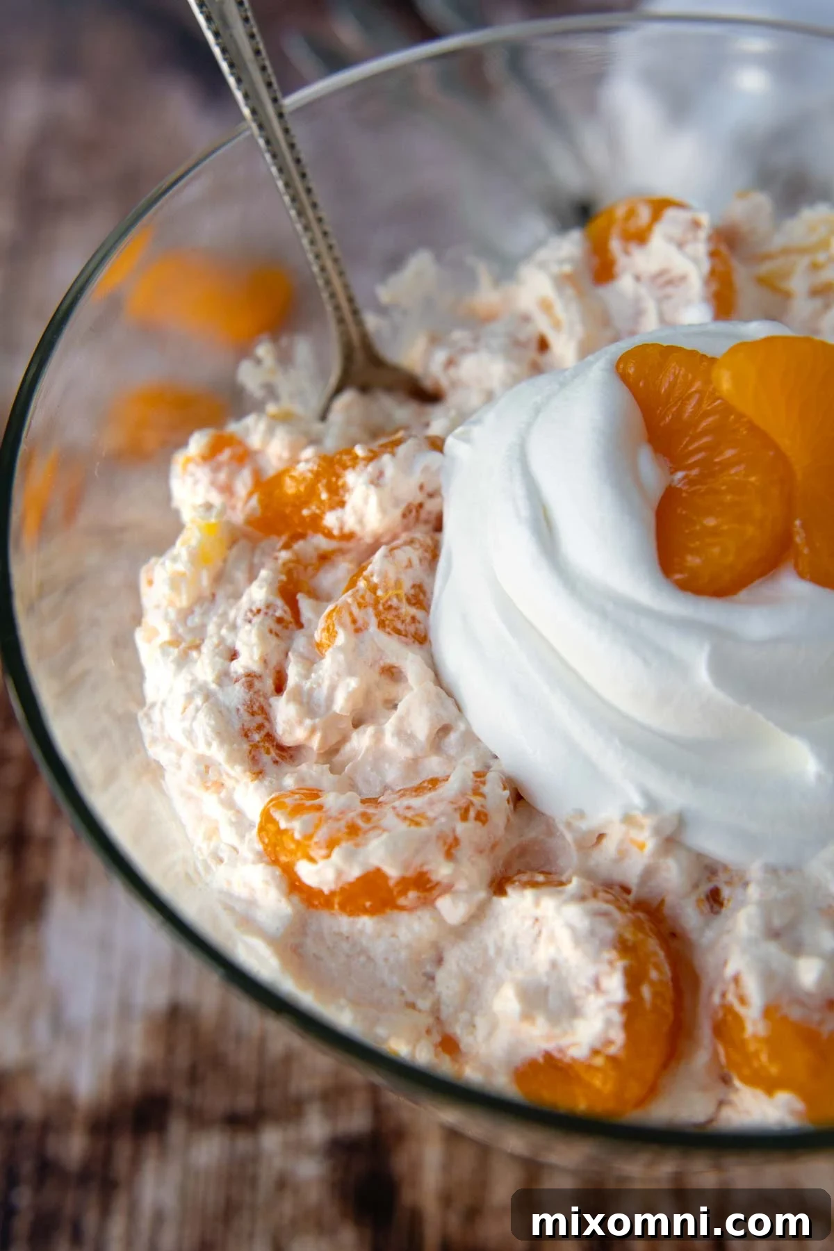 A close-up of the fluffy top of an orange Jello salad, adorned with a swirl of whipped cream.