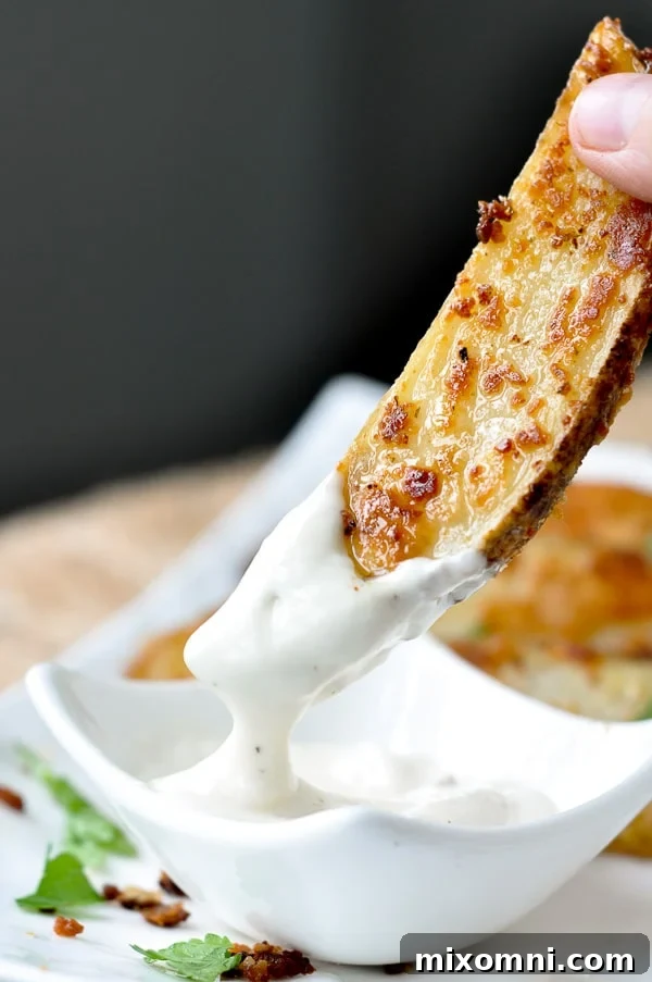 A perfectly roasted ranch potato wedge being dipped into a creamy bowl of ranch dressing, highlighting its golden crispiness.