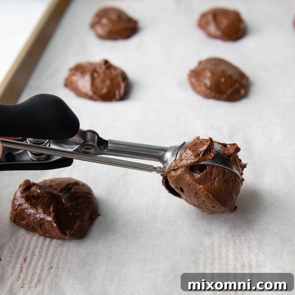 a cookie scoop placing the dough on a baking sheet.