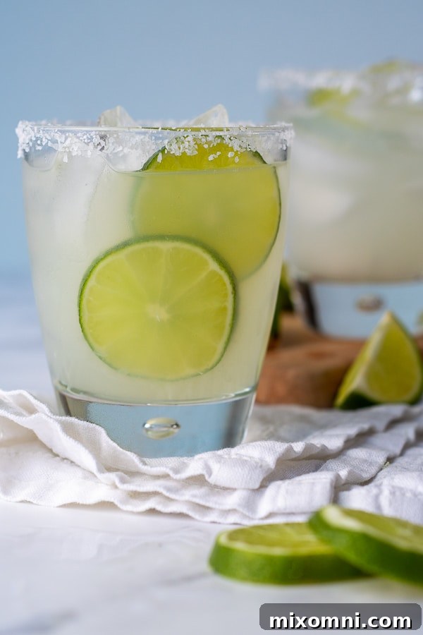A straight-on shot of a refreshing limeade margarita, with lime slices artfully arranged beside the glass