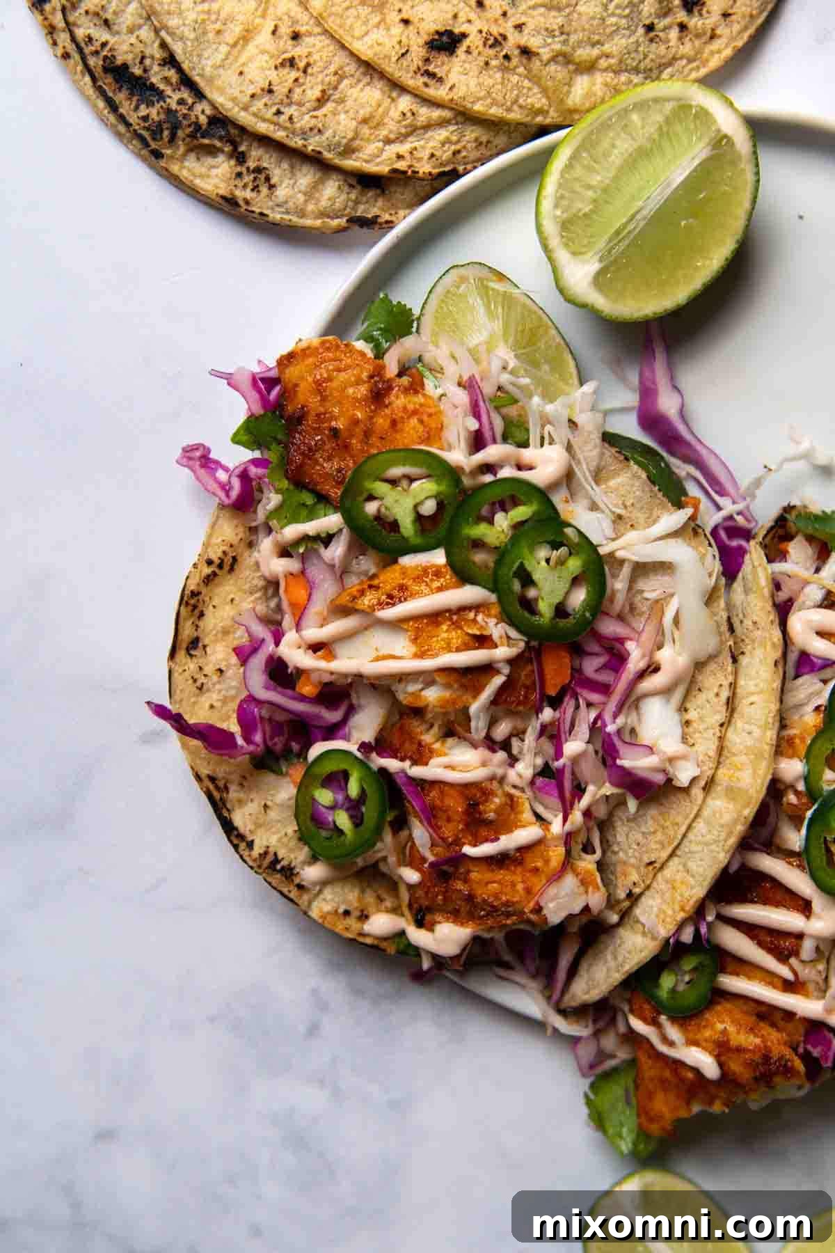 Overhead shot of beautifully plated blackened fish tacos surrounded by fresh lime wedges and vibrant garnishes