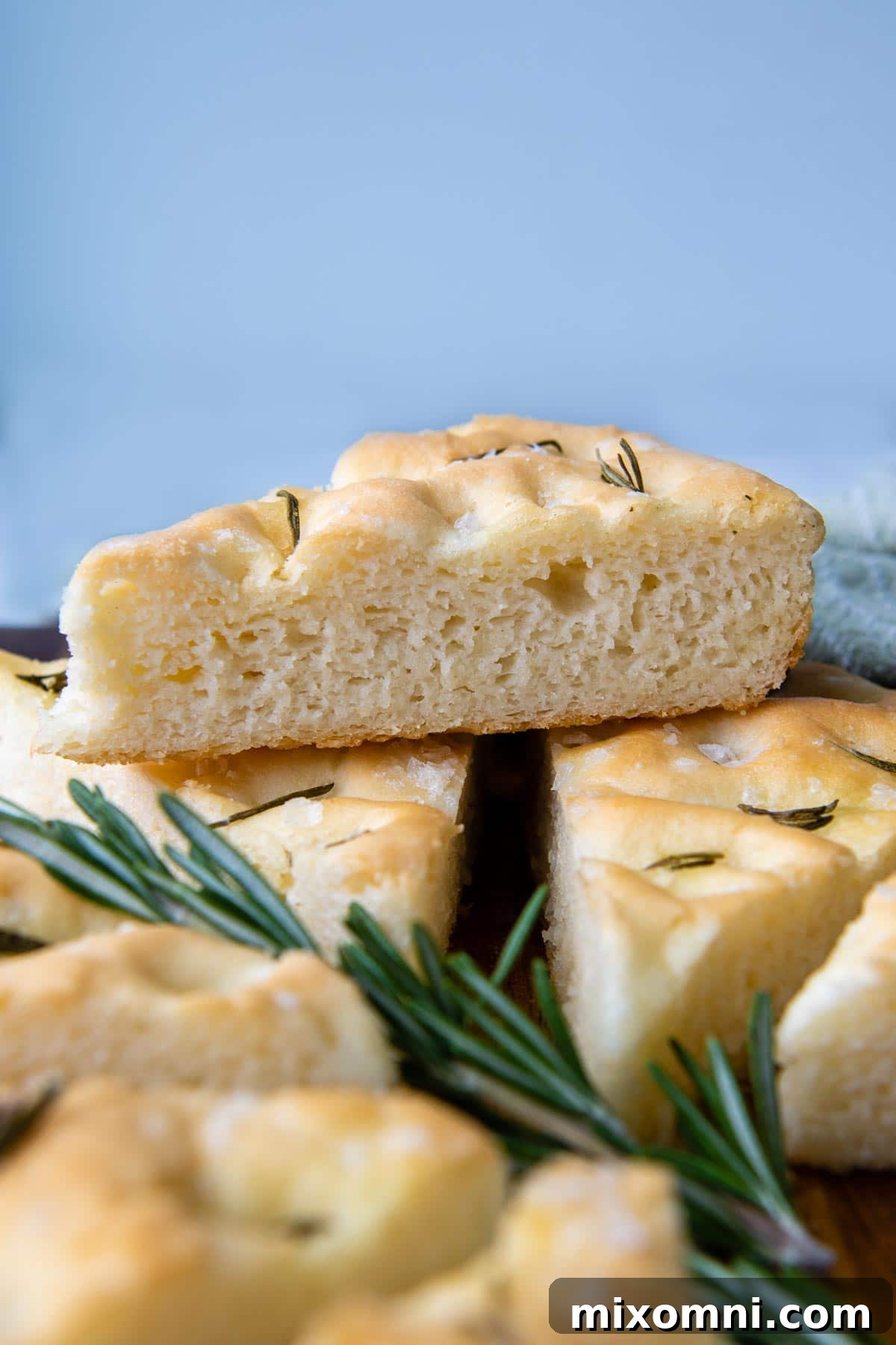 a slice of focaccia resting on other slices with fresh rosemary under