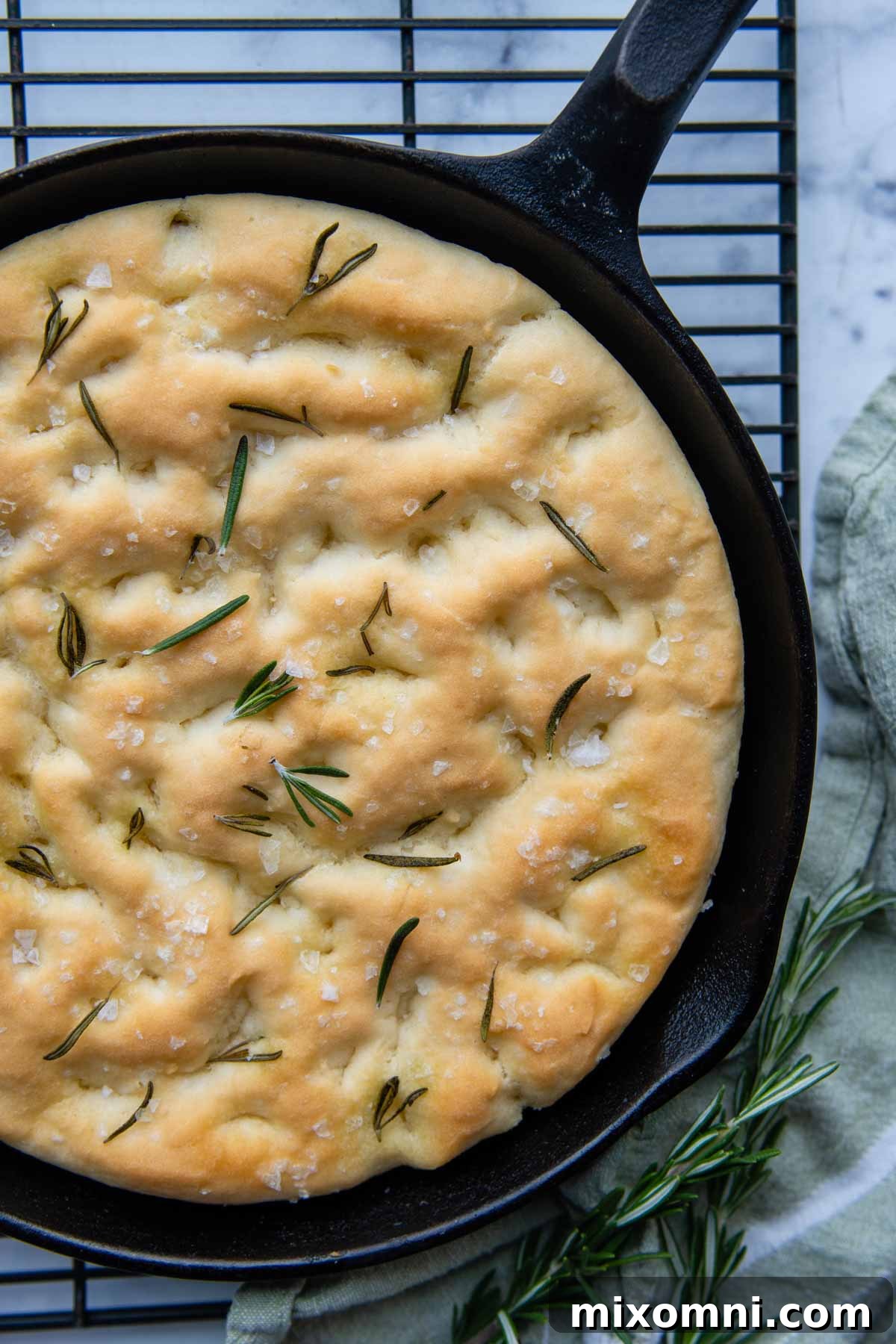 unsliced focaccia in a cast iron skillet on wire rack.