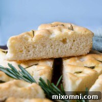 a slice of focaccia resting on other slices with fresh rosemary under