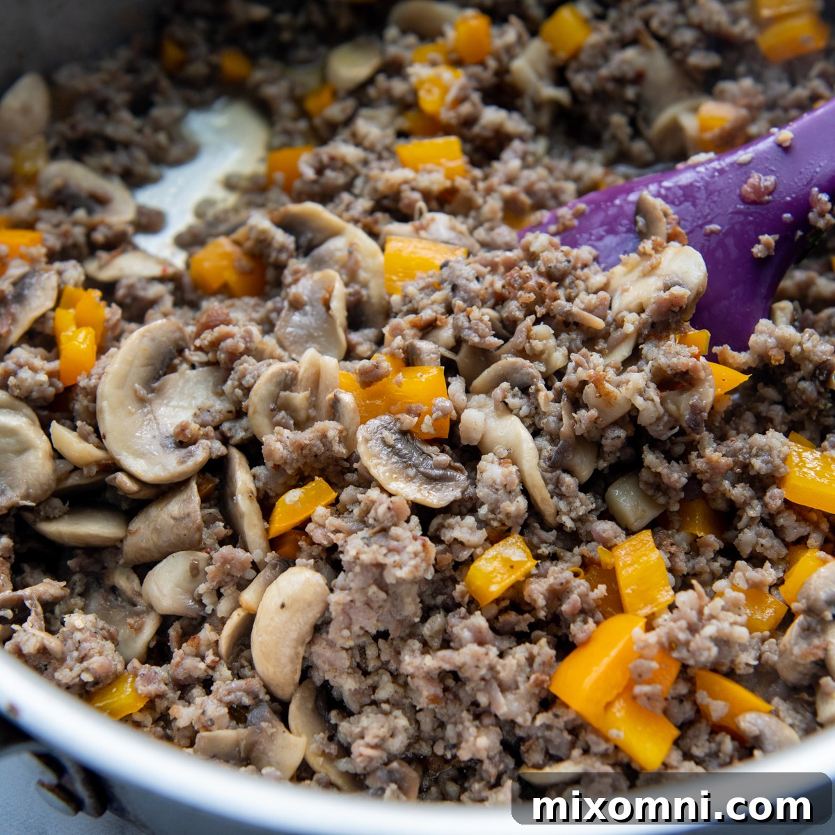 Sausage, mushrooms, and peppers cooking in a skillet, creating a fragrant base for the quiche.