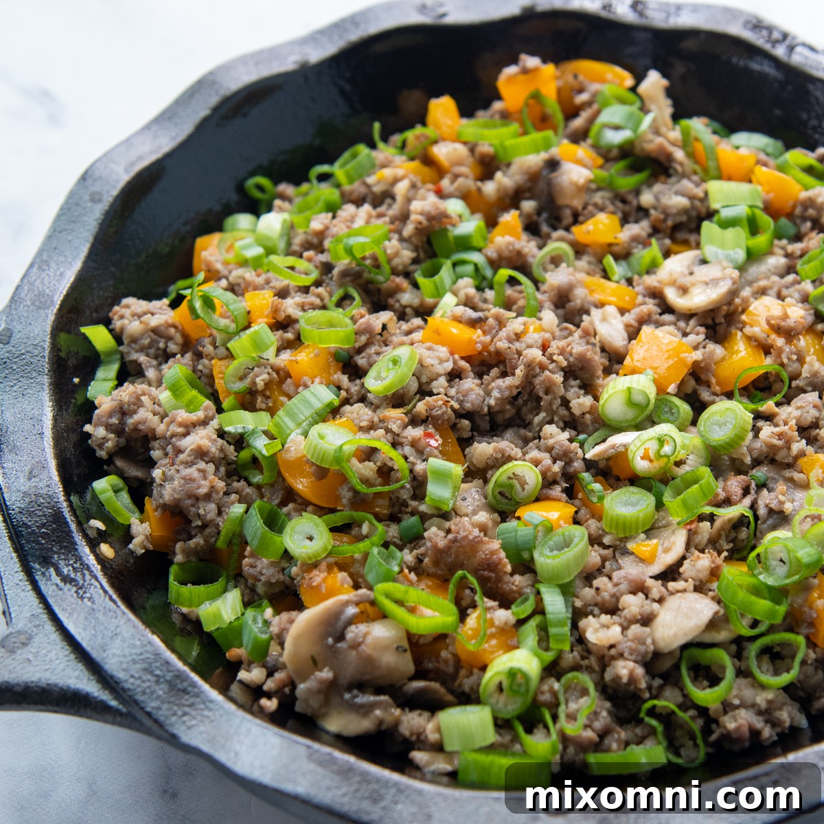 The sautéed sausage and vegetable mixture, topped with vibrant green onions and cheese, arranged in a pie plate.