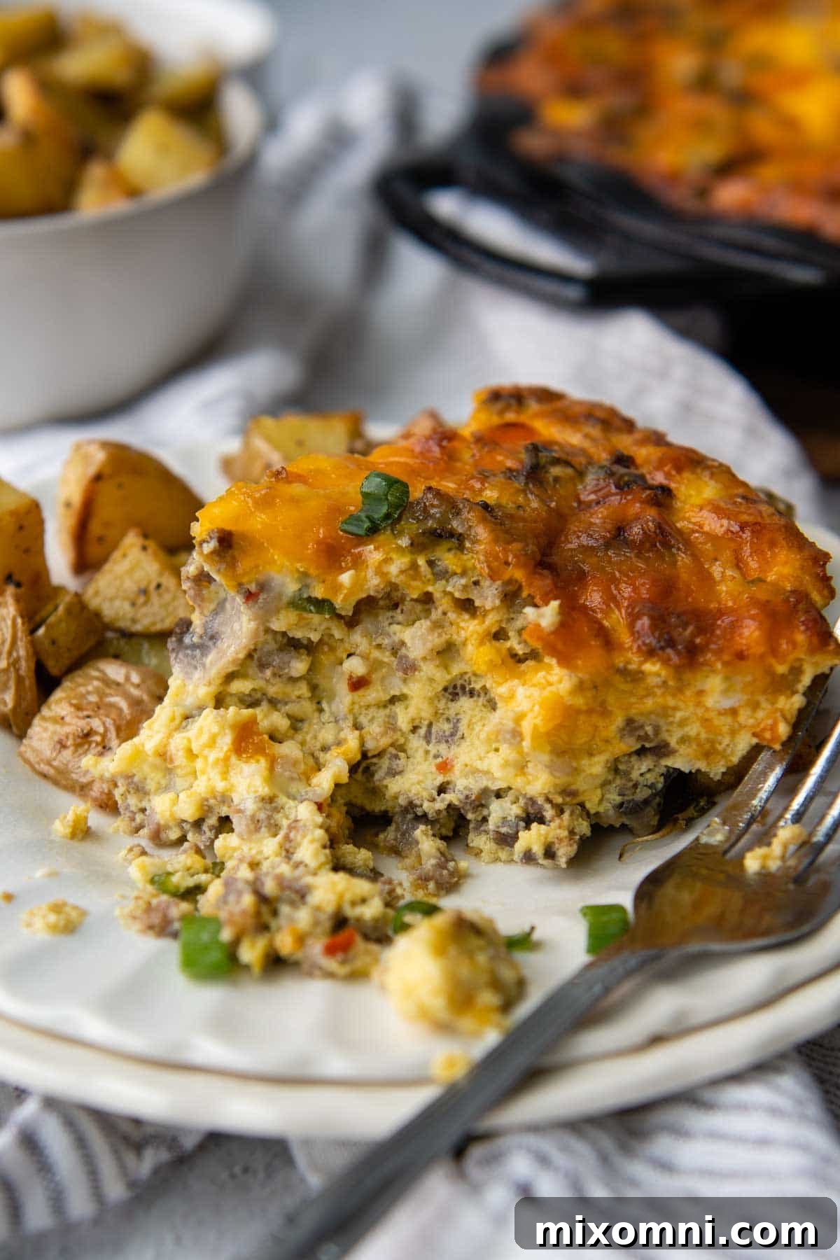 A delicious slice of crustless quiche on a white plate with a fork, showing the creamy texture and hearty fillings.