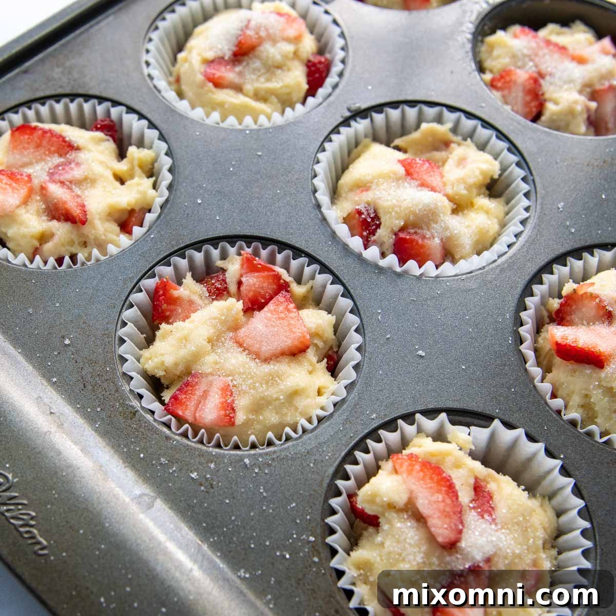 unbaked muffins in a muffin pan with sugar sprinkled on the tops.