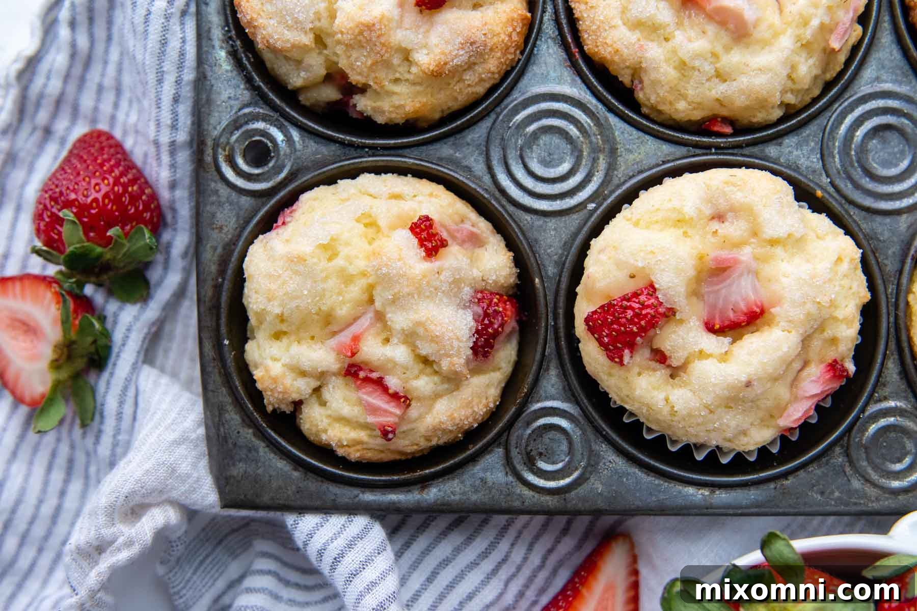 An overhead shot of two muffins in a vintage muffin pan with fresh strawberries next to it.