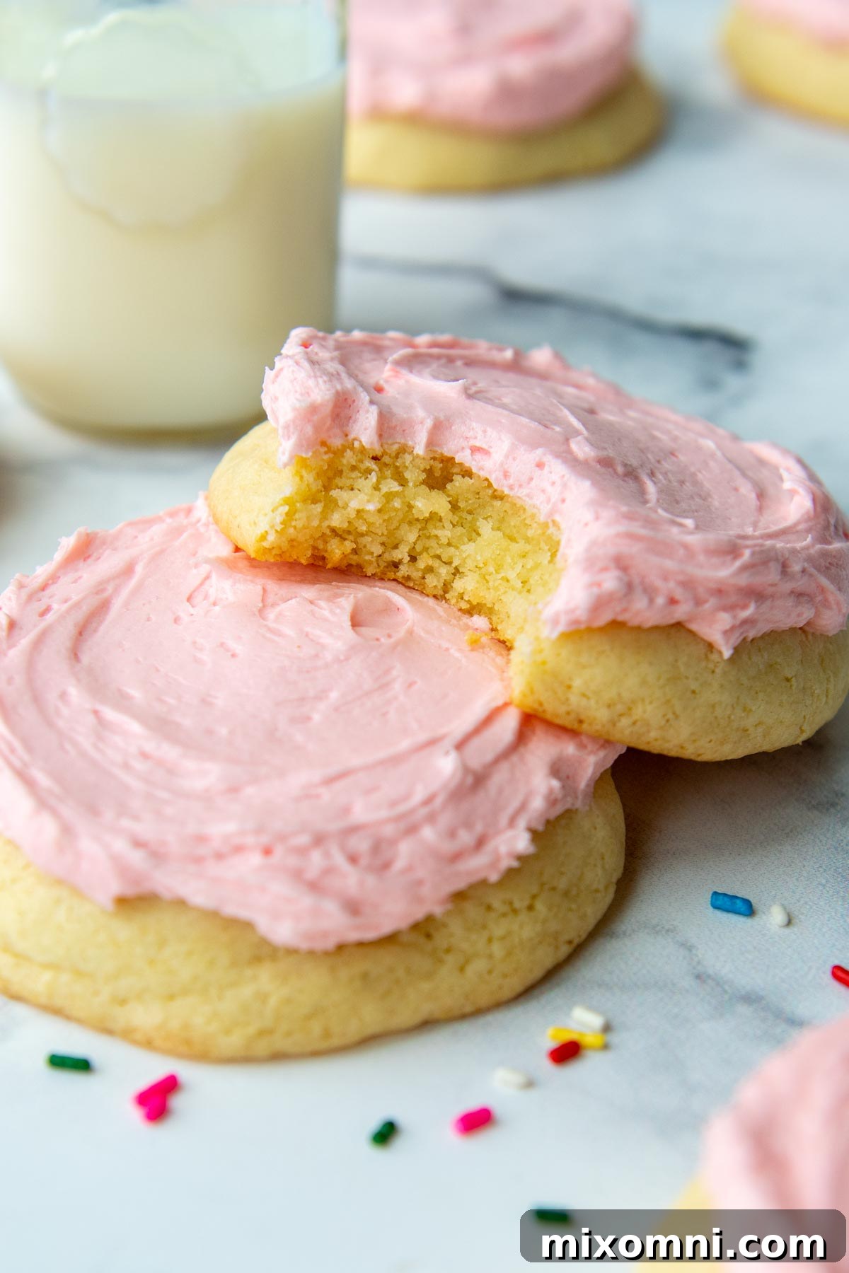 Two frosted sugar cookies, one with a bite taken out, resting stacked on top of each other, showcasing their soft interior.