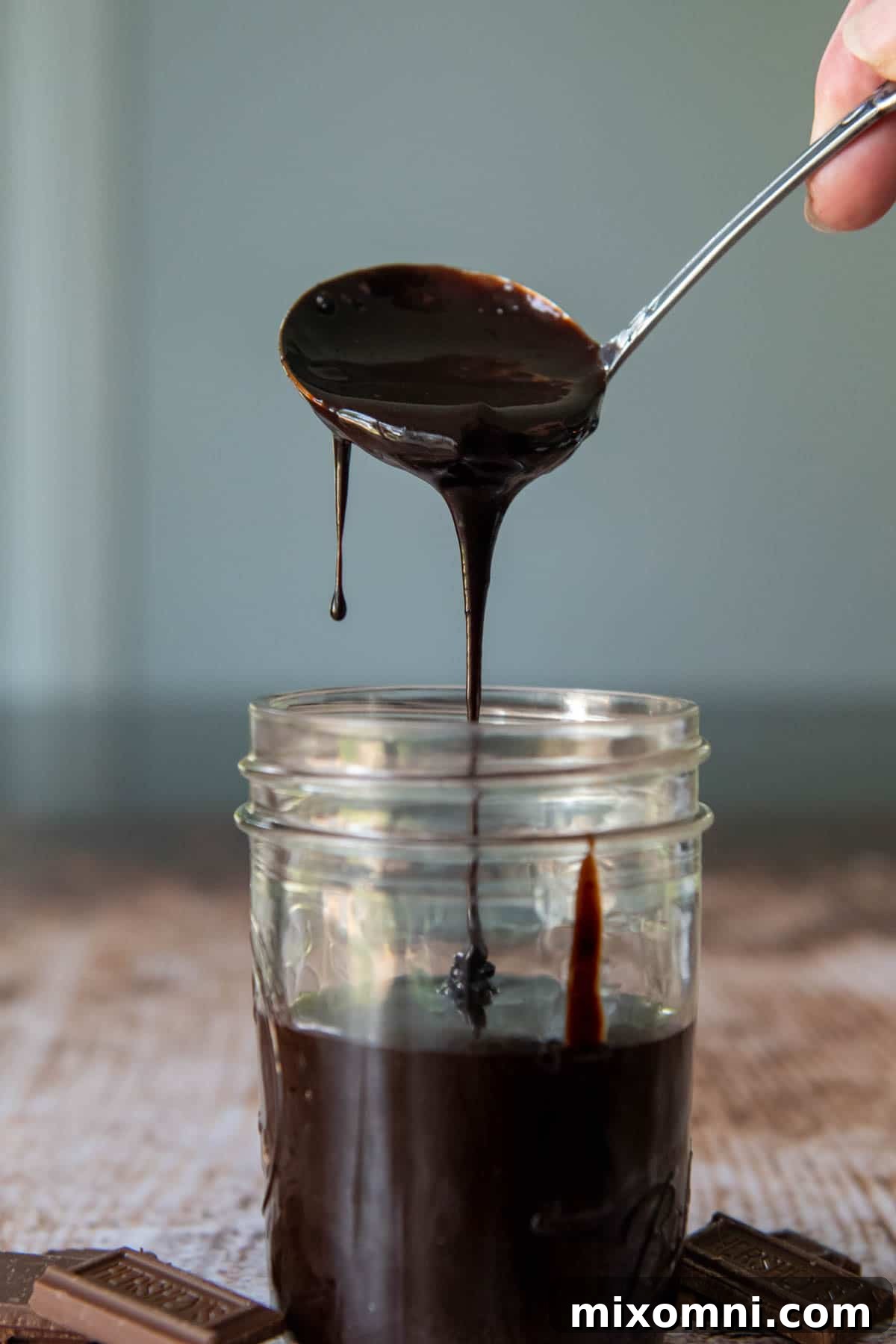 a ladle scooping in hot fudge sauce into a glass jar