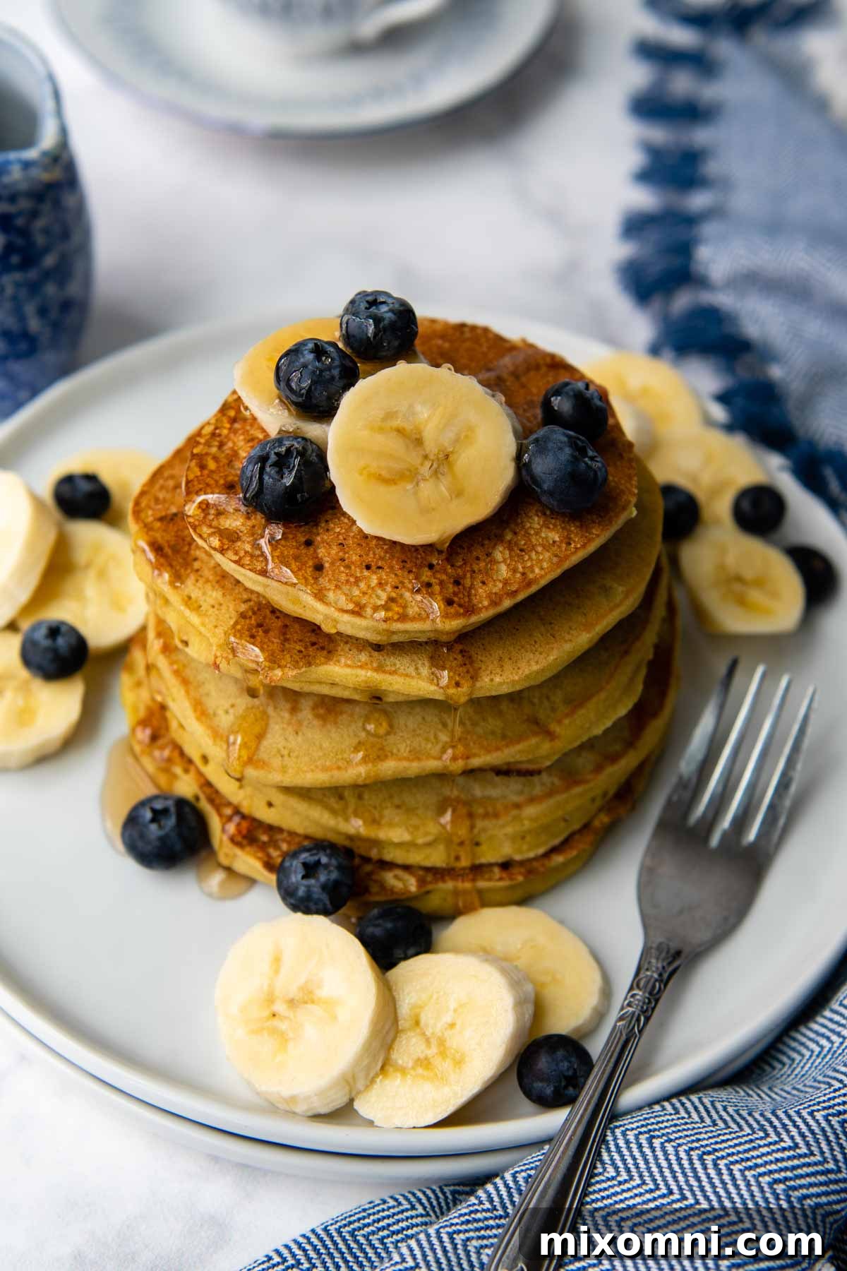 An overhead shot showcasing a beautiful stack of buckwheat banana pancakes, generously topped with fresh blueberries and banana slices, ready to be enjoyed.