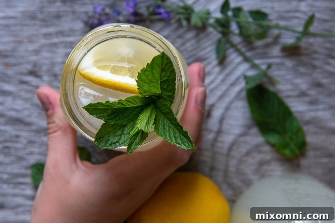 Overhead shot of a hand reaching for a vodka lemonade cocktail garnished with fresh mint in a glass.