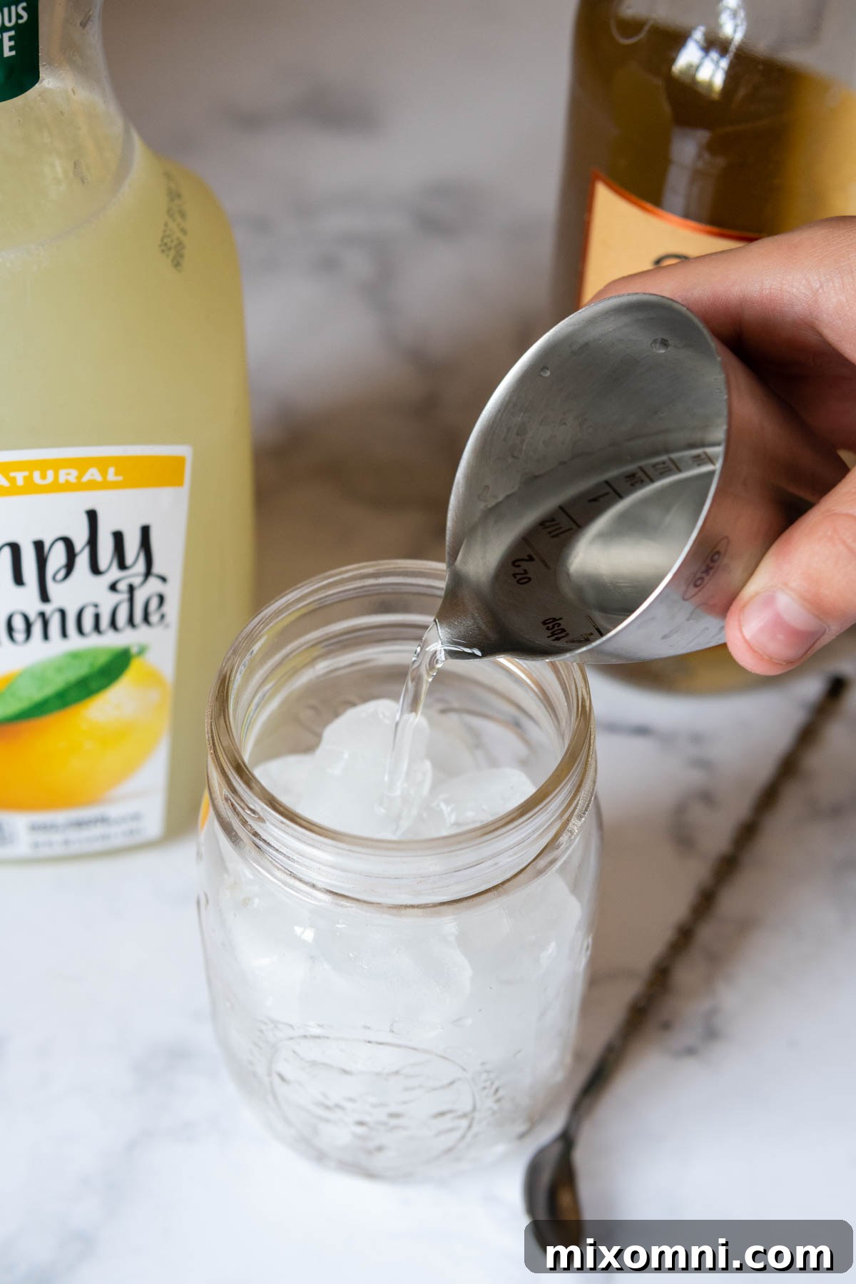 Vodka being poured into a glass filled with ice and lemonade.