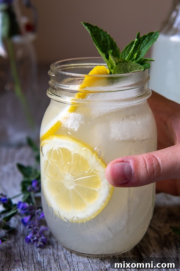 A hand reaching to pick up a jar glass of vodka and lemonade, garnished with a lemon slice.