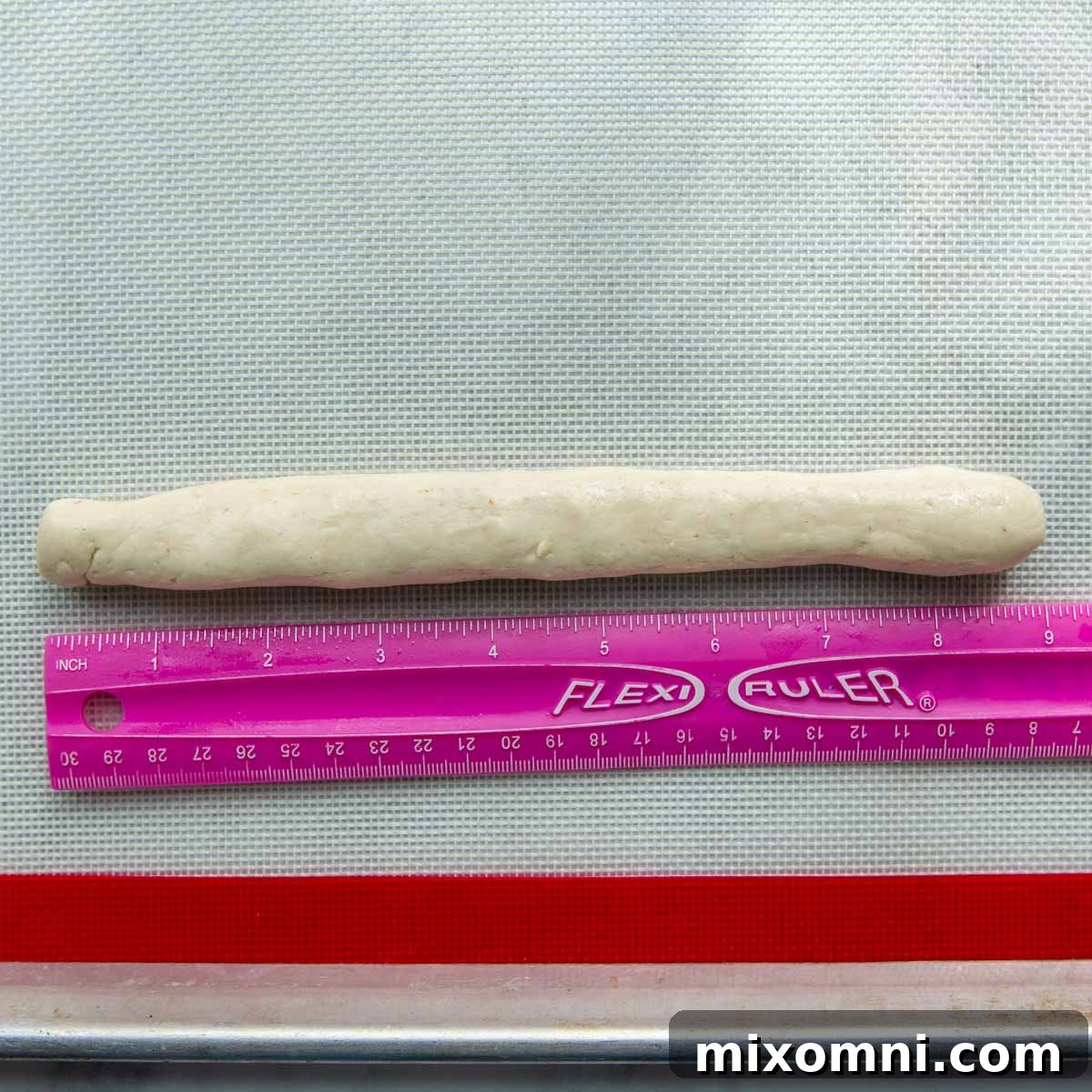 The gluten-free dough rolled out into a uniform 9-inch rope, with a ruler demonstrating its length, illustrating the preparation for tying into knots.
